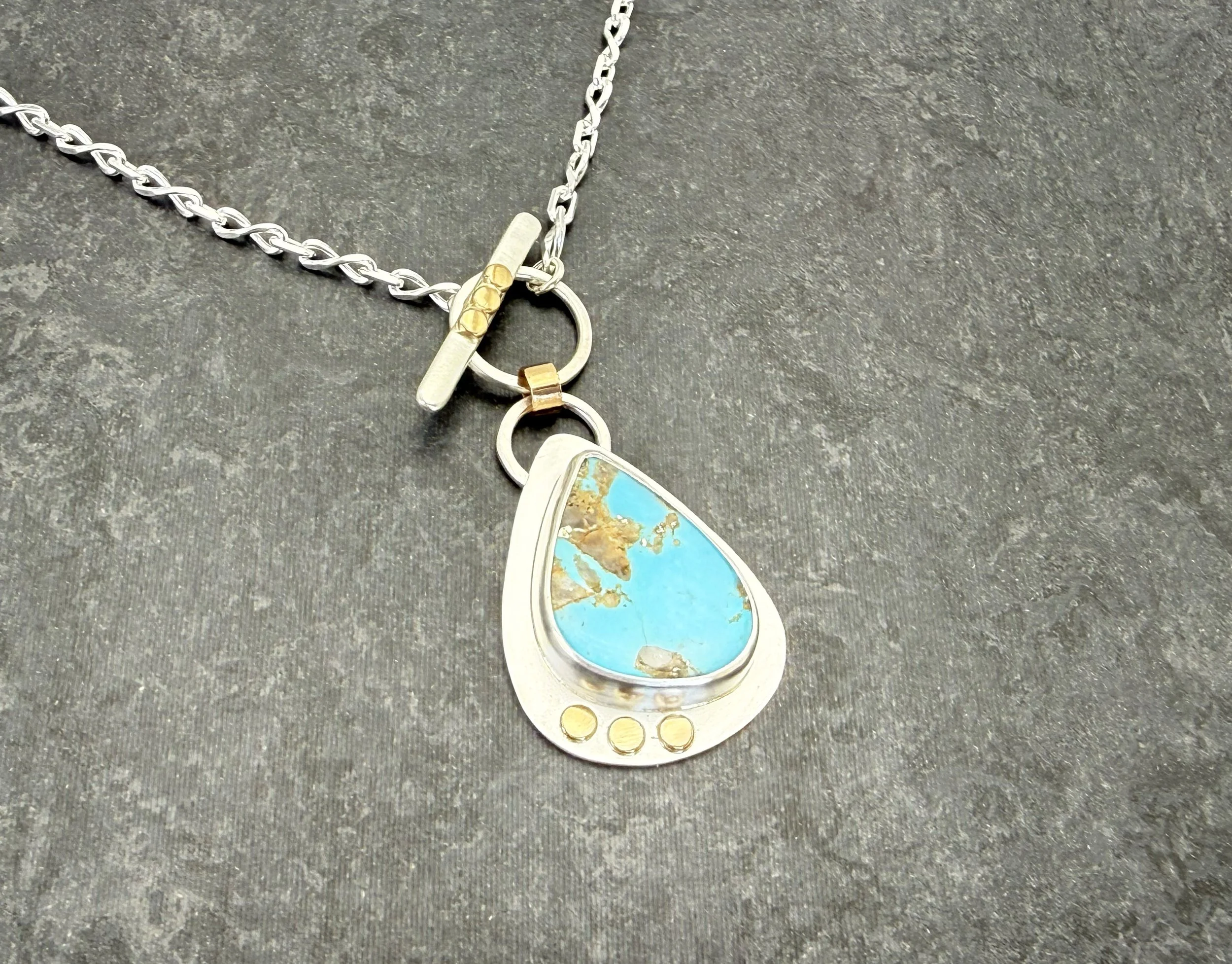 Turquoise teardrop pendant and 14k gold toggle on gray slate