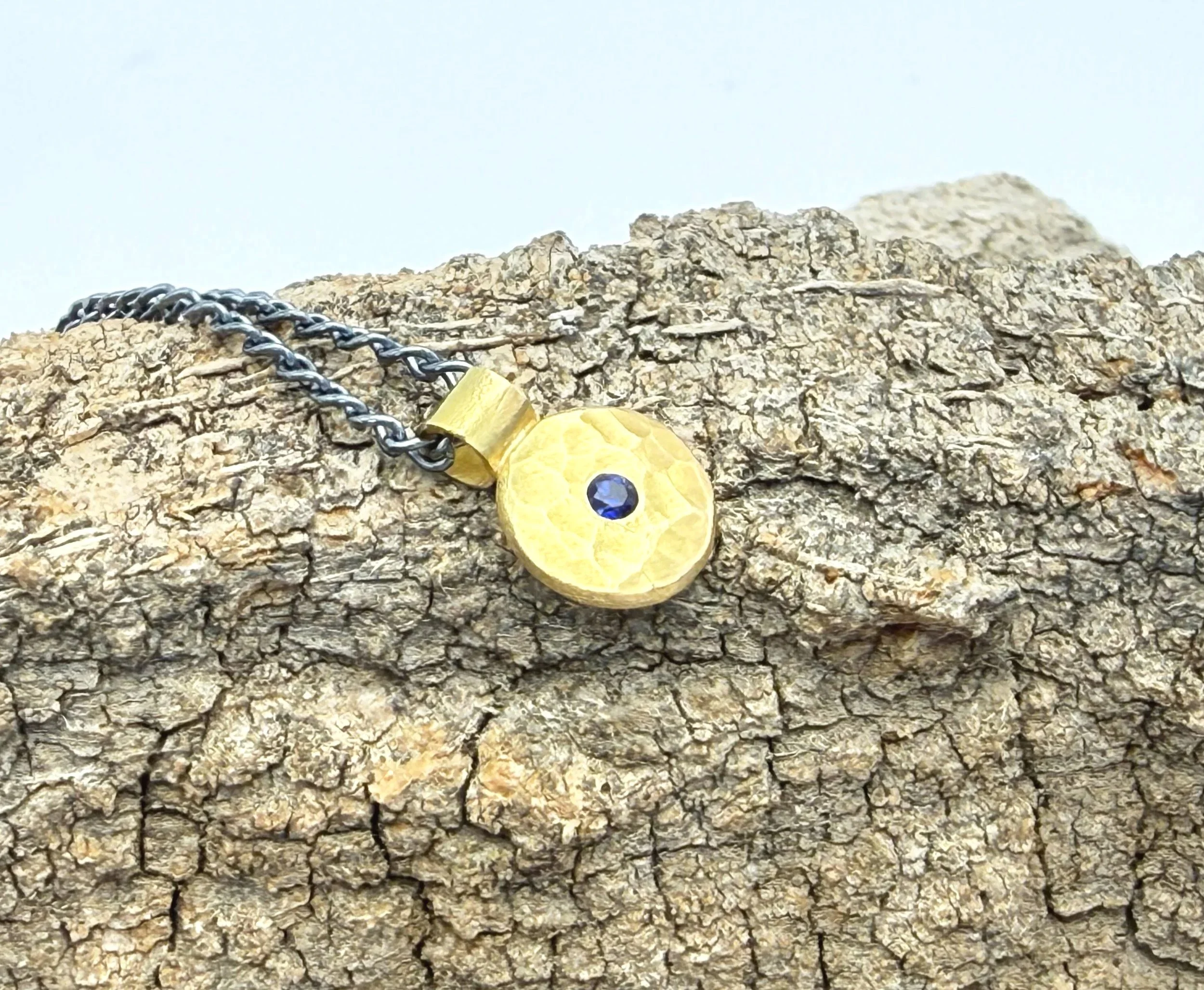 Hammer-textured gold disc pendant with sapphire on textured stone