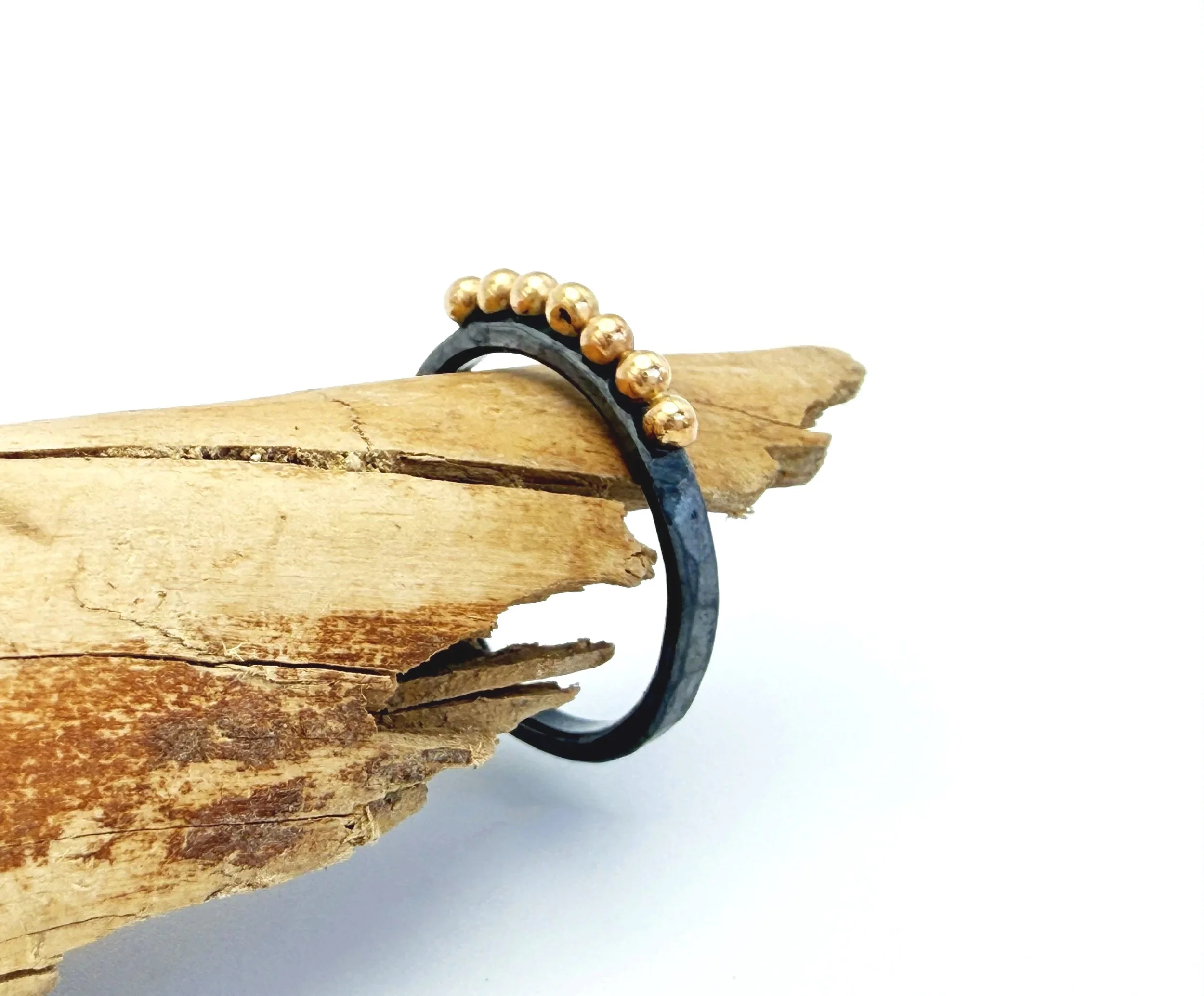Dark oxidized silver band with 14k gold dots, standing on driftwood