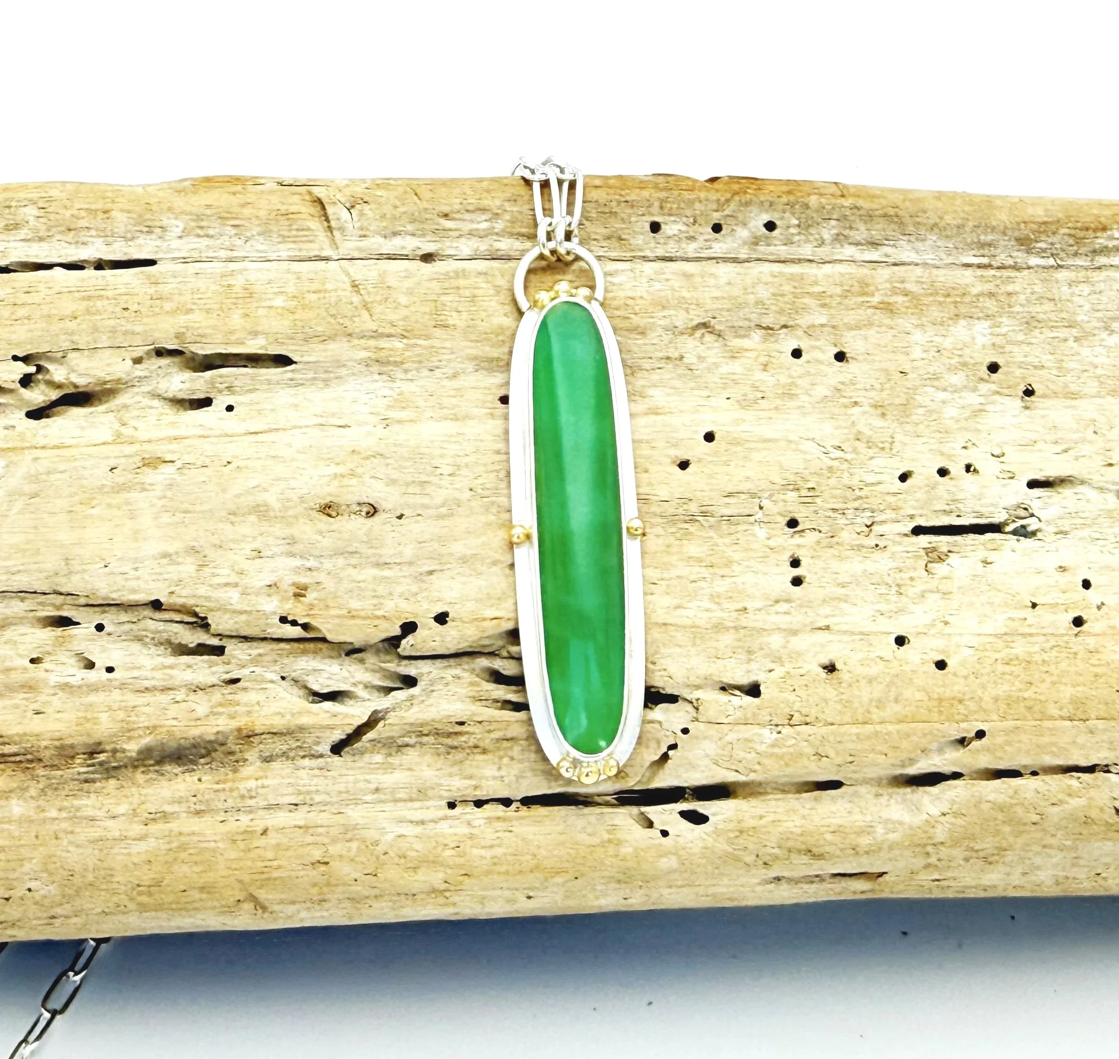 Elongated apple green chrysoprase pendant in a sterling silver bezel, on driftwood
