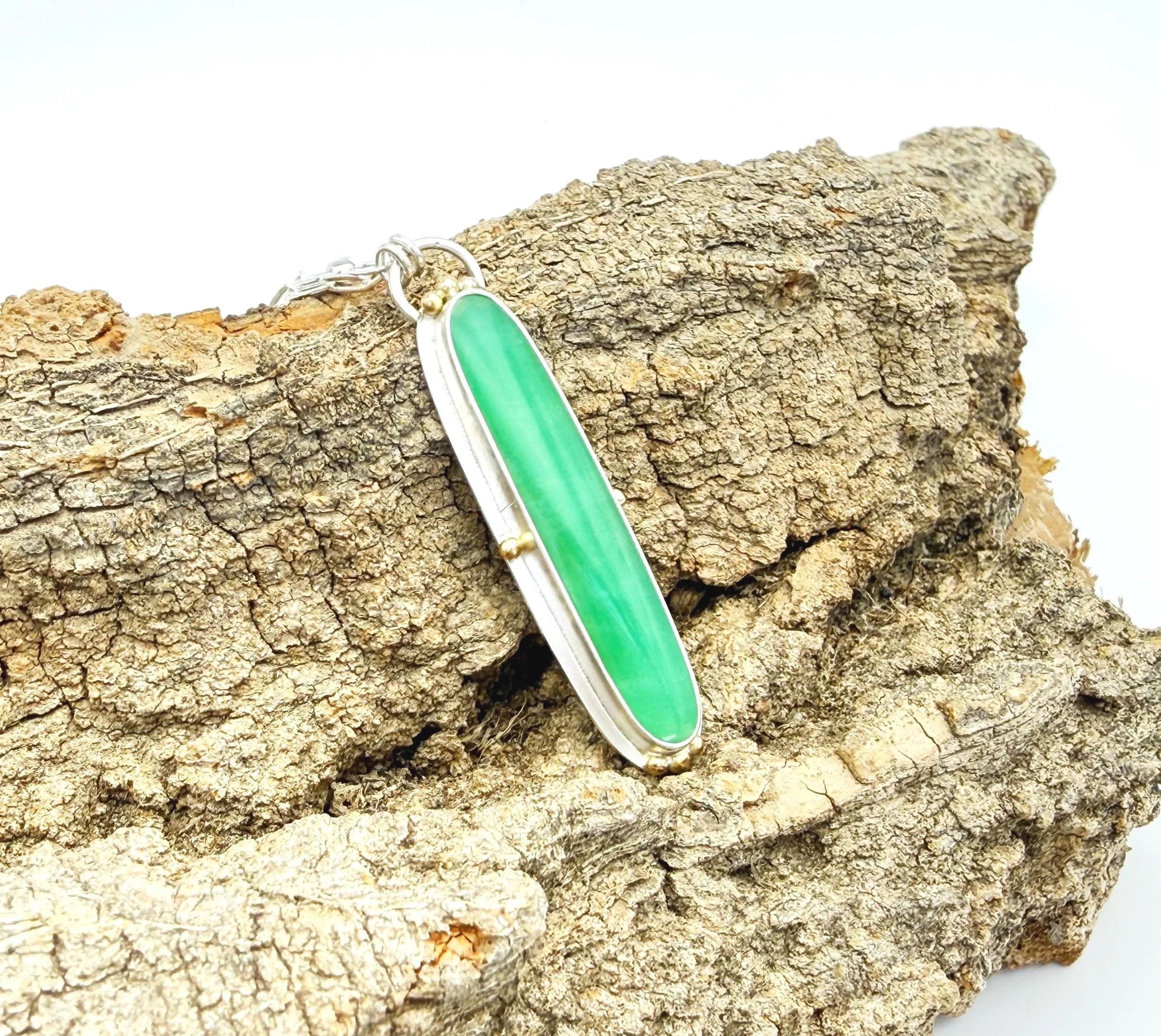 Chrysoprase pendant with 14k gold dots resting on weathered stone