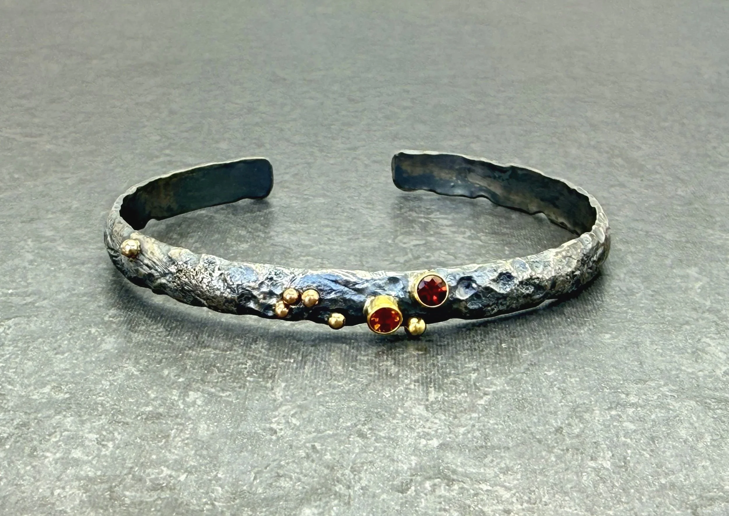 Oxidized silver cuff with garnet, citrine and gold dots on dark slate