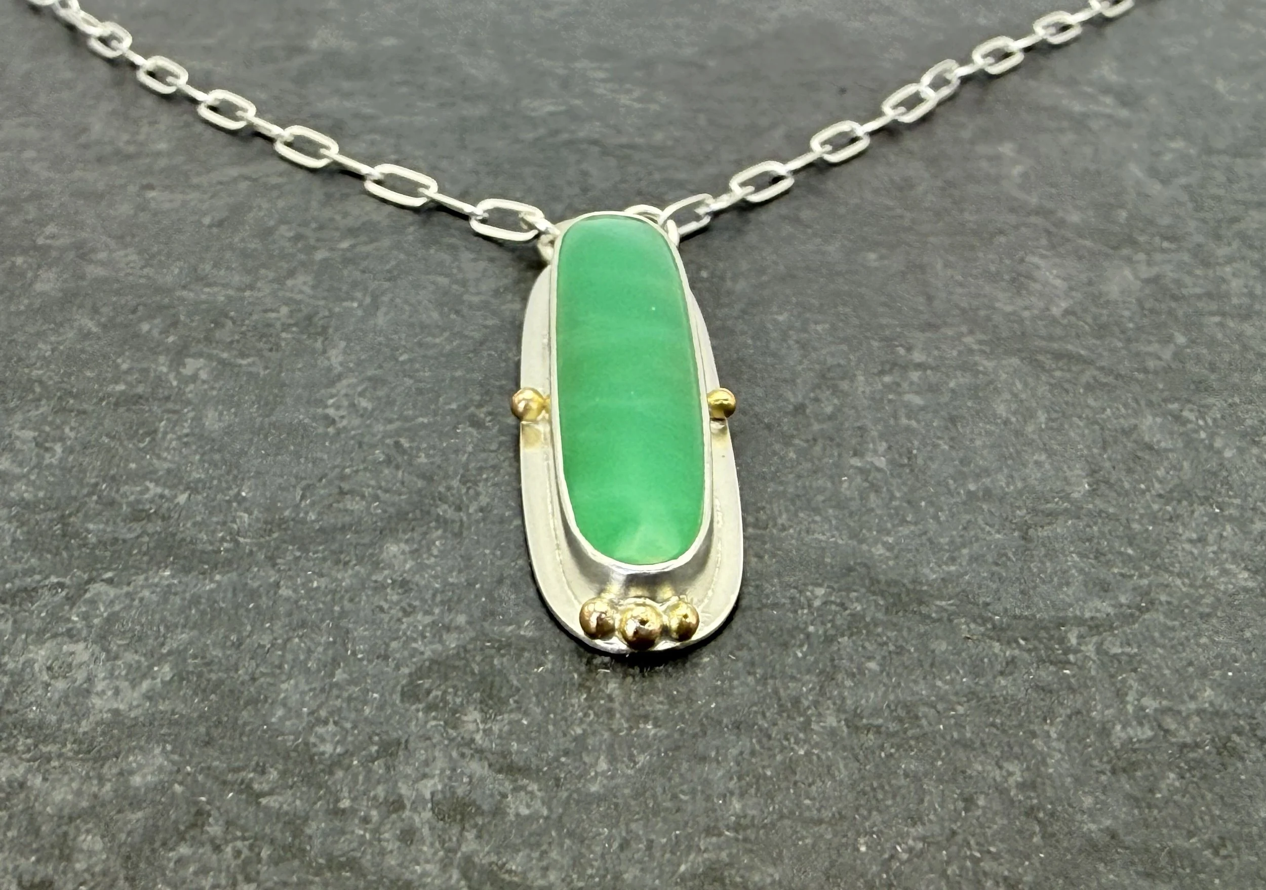 Chrysoprase pendant on a paperclip chain against dark slate
