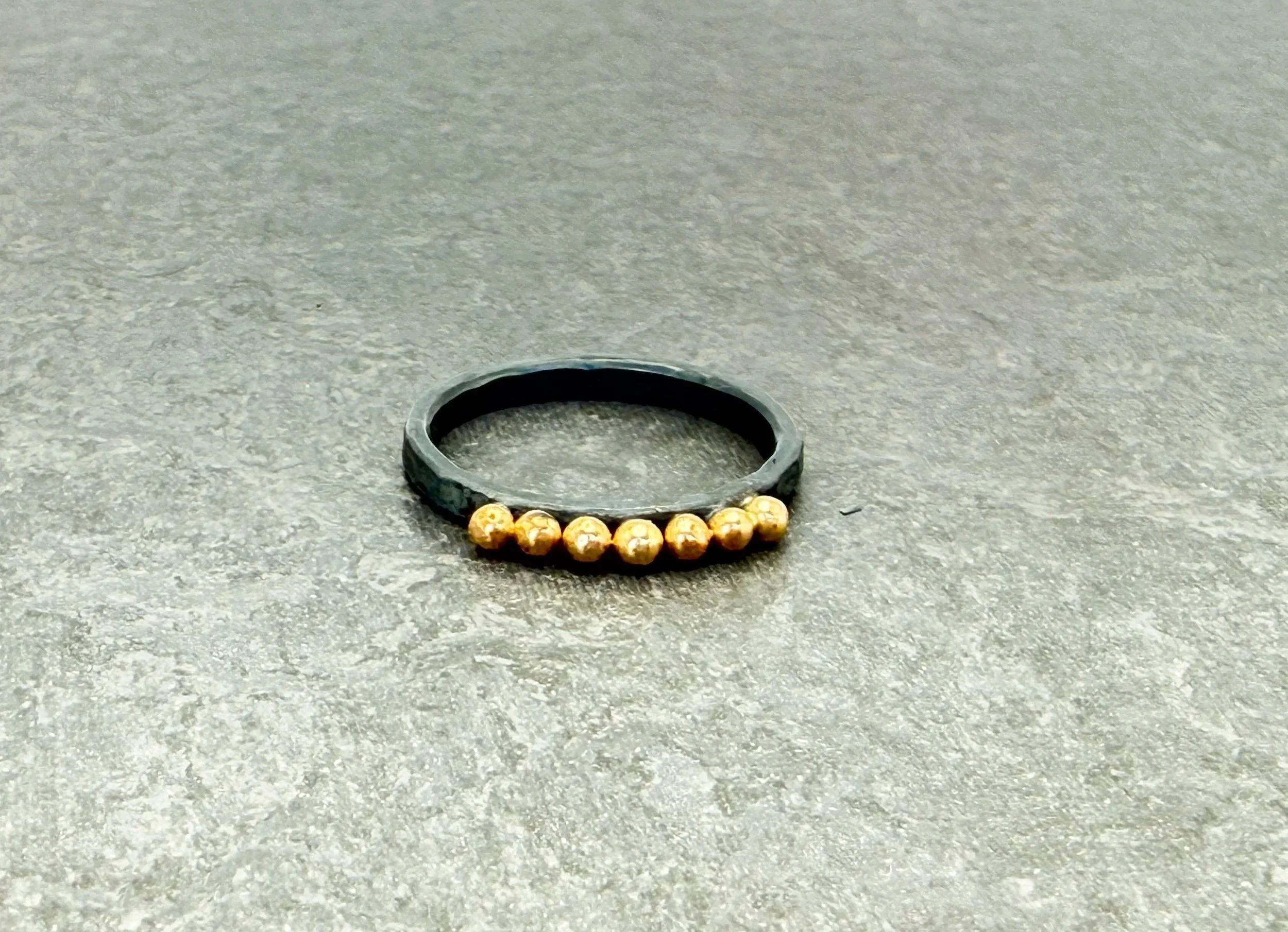 Charcoal gray oxidized silver ring with a row of 14k gold dots, on gray stone