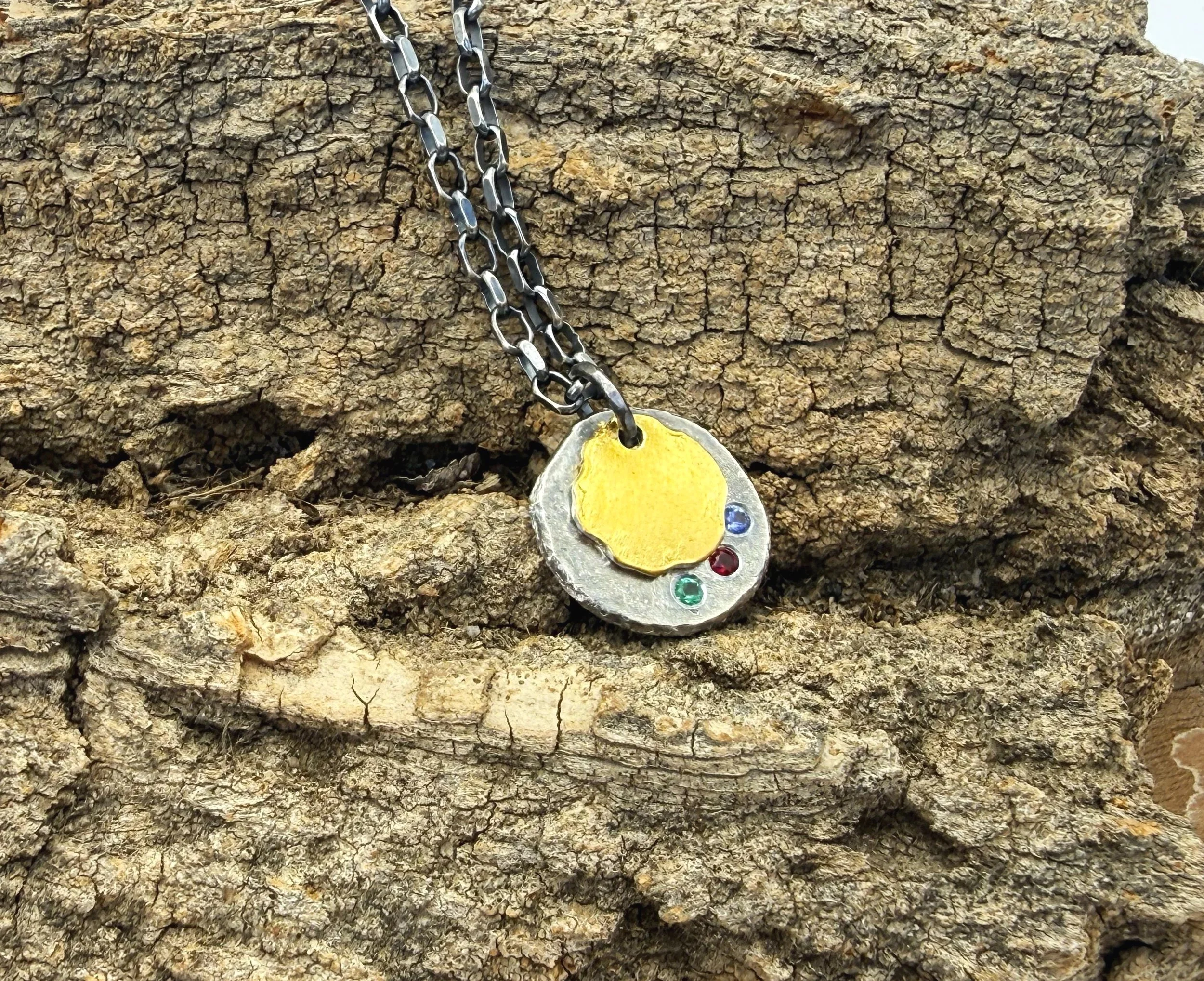 Oxidized silver disc necklace with 24k gold keum boo and three birthstones, on weathered wood