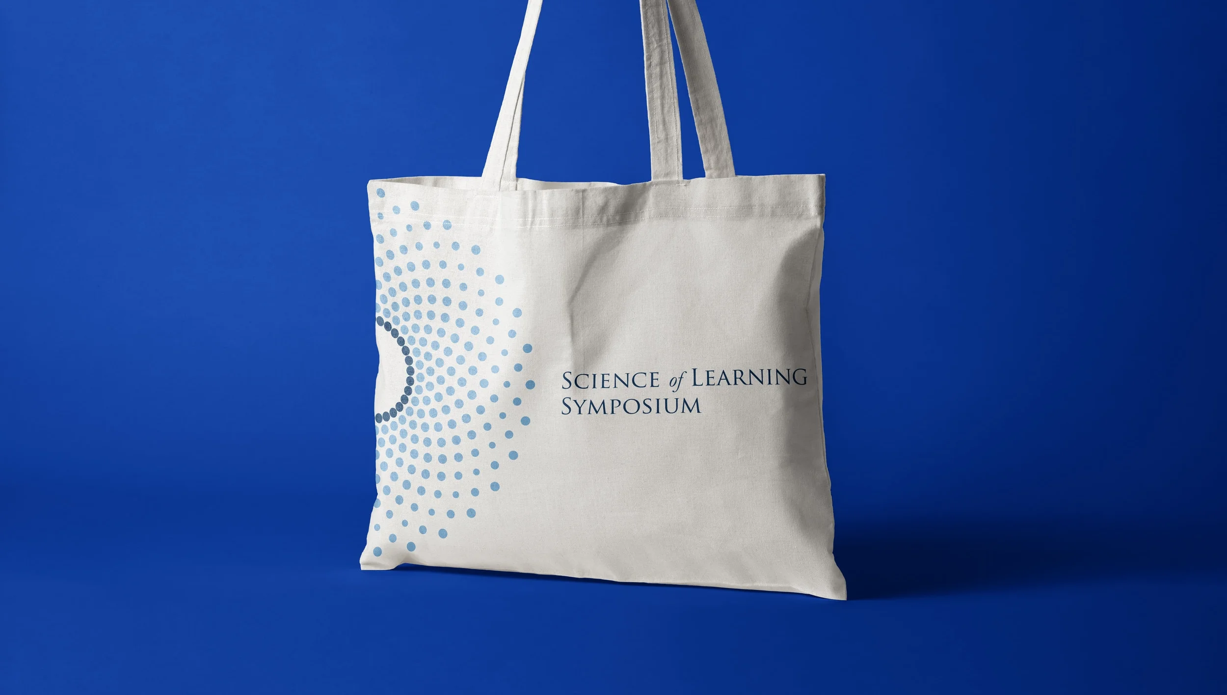 Tote bag with 'Science of Learning Symposium' and blue dotted spiral design on a blue background.