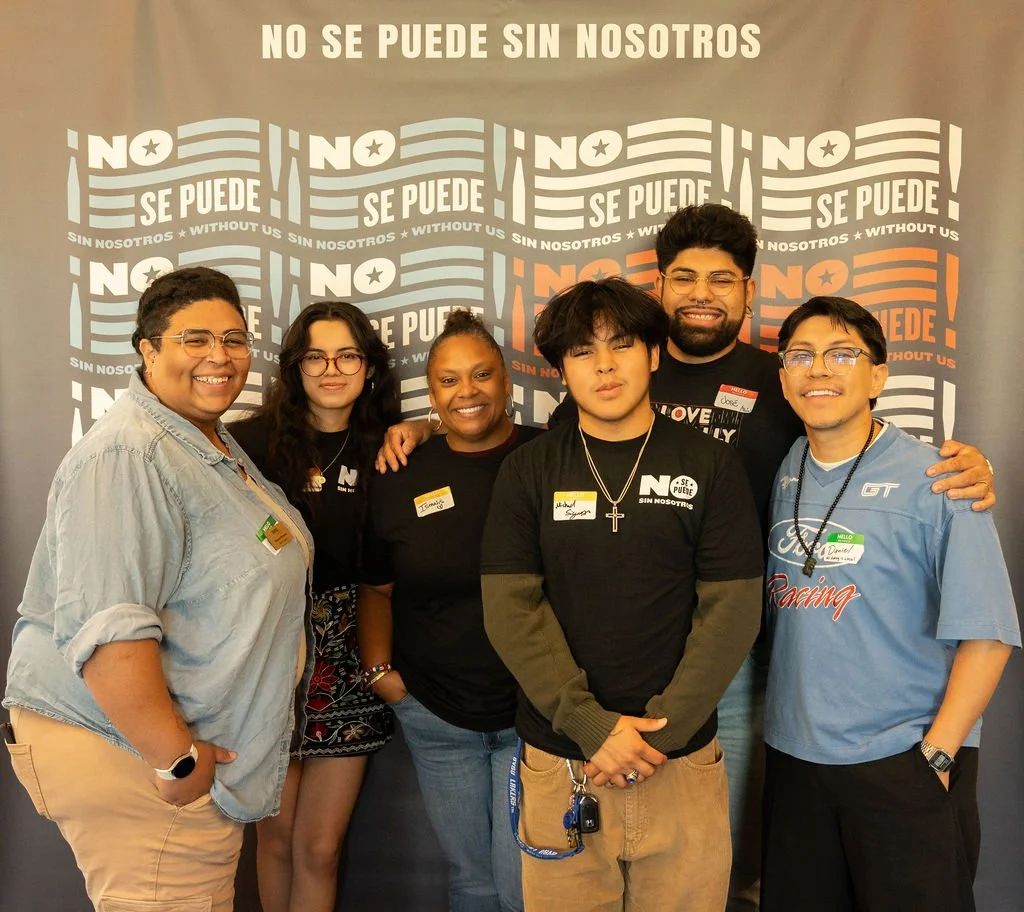 Group of six diverse people posing together in front of a backdrop with the text 'NO SE PUEDE SIN NOSOTROS' repeated multiple times.