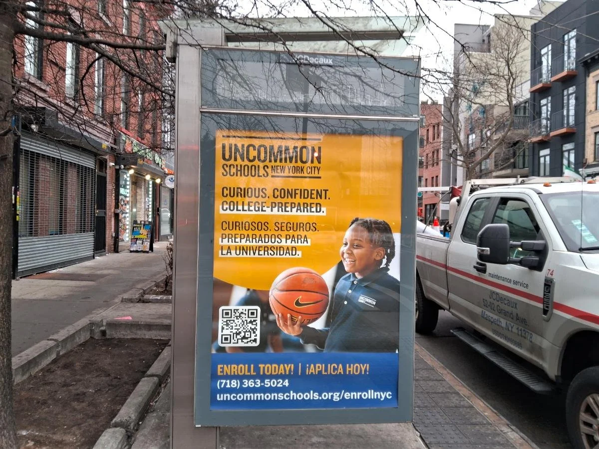 Poster advertising Uncommon Schools in New York City featuring a smiling young girl holding a basketball, with text in English and Spanish encouraging enrollment, a QR code, and contact information.