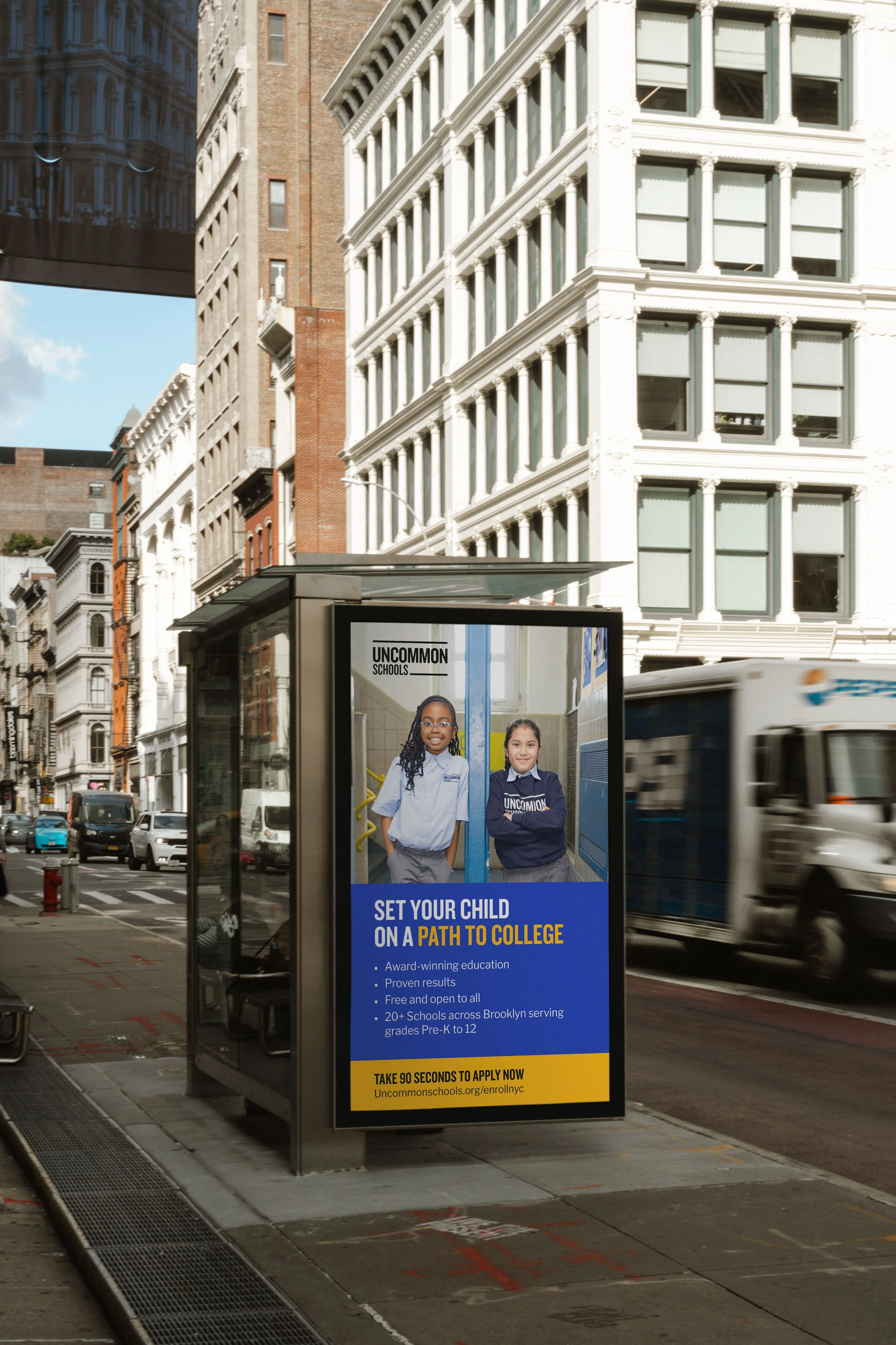 An outdoor advertisement on a bus shelter promoting education for children, featuring two smiling girls in school uniforms, with a background of office buildings and city streets.