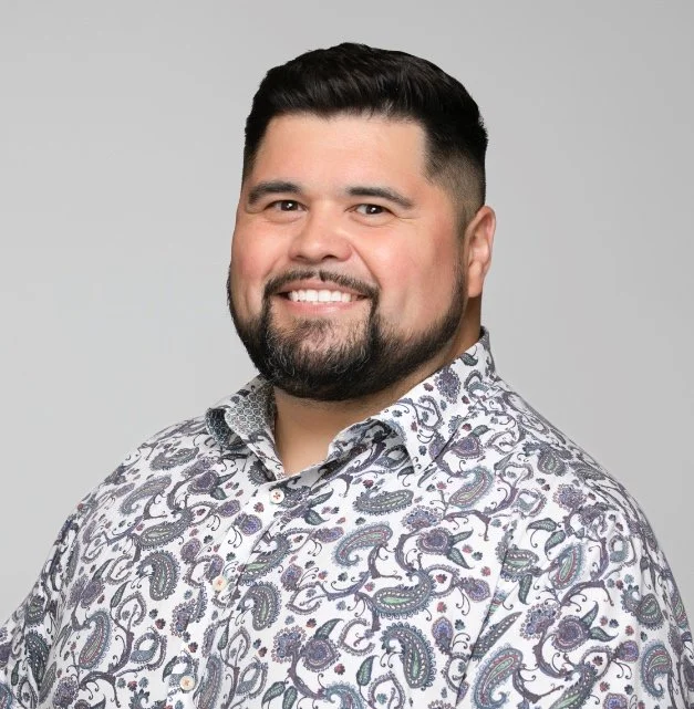 Smiling man wearing a paisley-patterned shirt on a gray background.