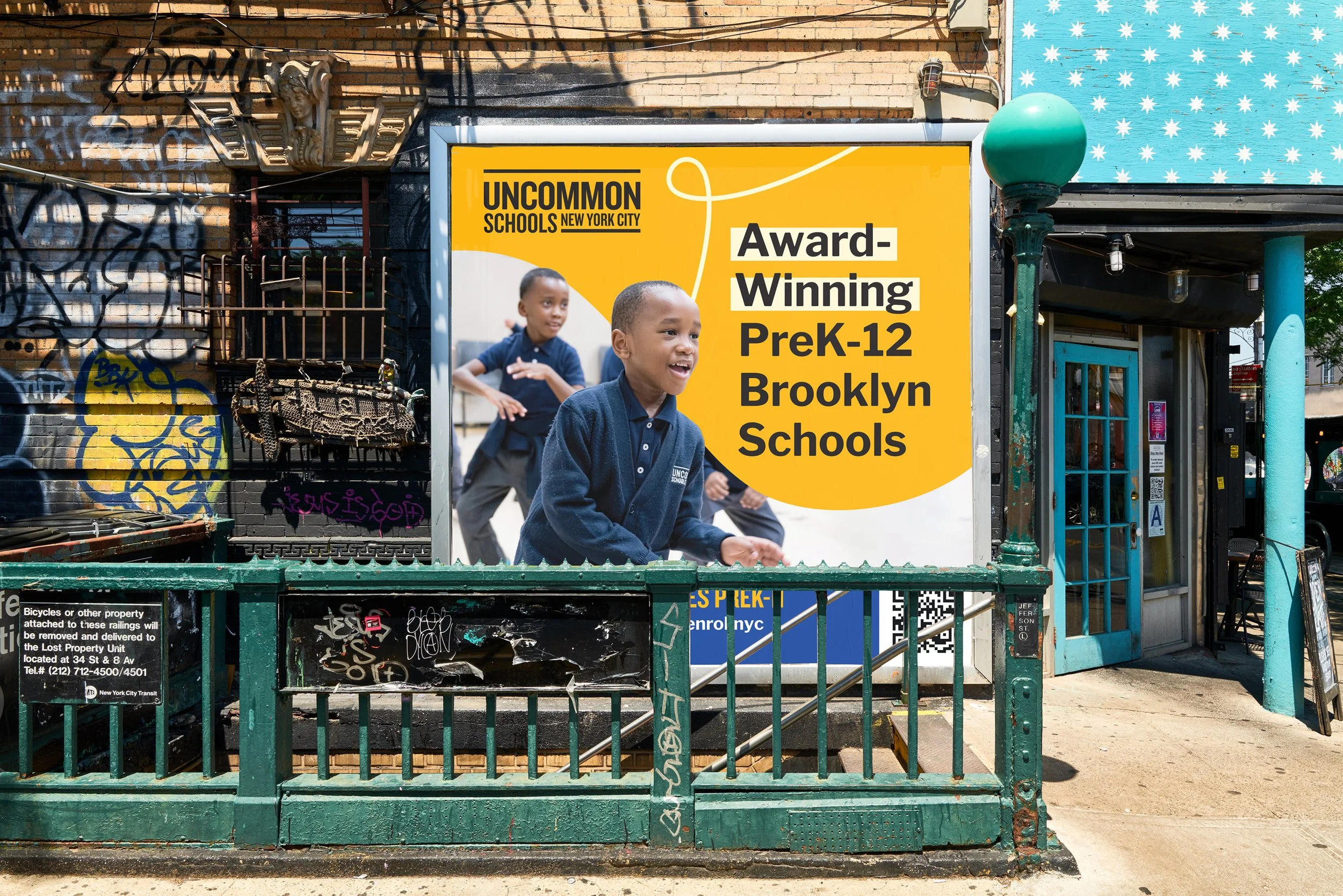 Billboard advertising Uncommon Schools Brooklyn PreK-12, featuring children playing, against a graffiti-covered wall and urban street scene.