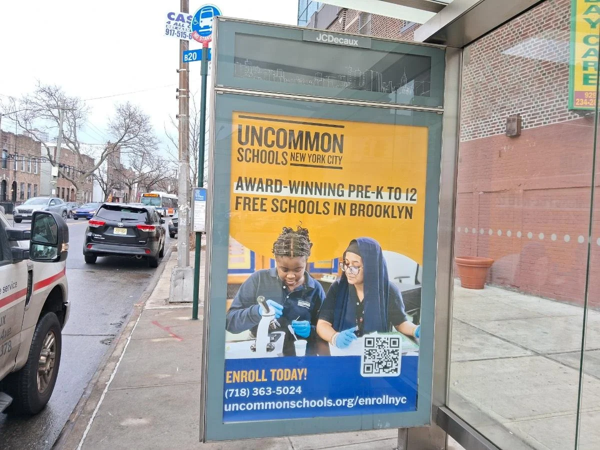 A bus stop advertisement for UnCommon Schools in Brooklyn, New York, offering free pre-K to 12 education, with images of students doing science activities and text providing contact information and a QR code.
