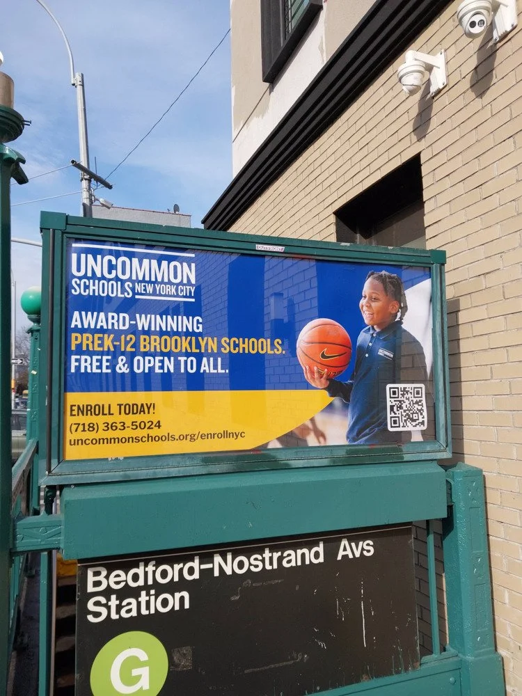 An advertisement on a bus stop shelter for Uncommon Schools New York City, promoting free pre-kindergarten to K-12 Brooklyn schools. It features a smiling young girl holding a basketball, with a QR code and contact information for enrollment.