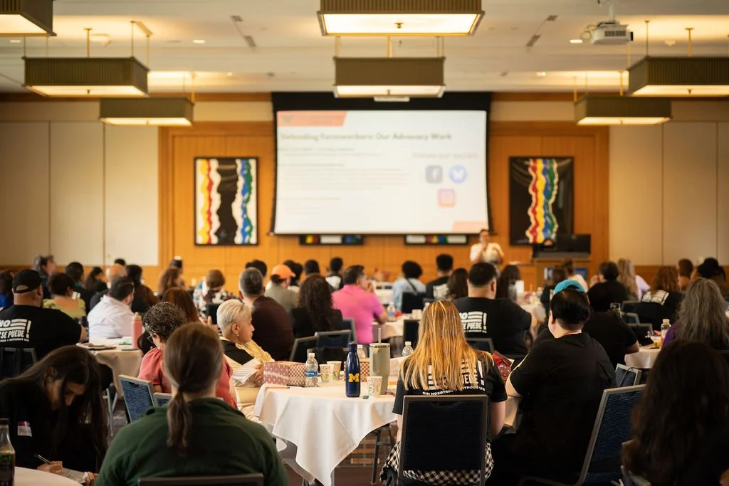 A large conference room filled with people seated at round tables, attending a presentation with a large screen at the front displaying a slide titled 'Understanding Treatment: Our Anniversary Week.'