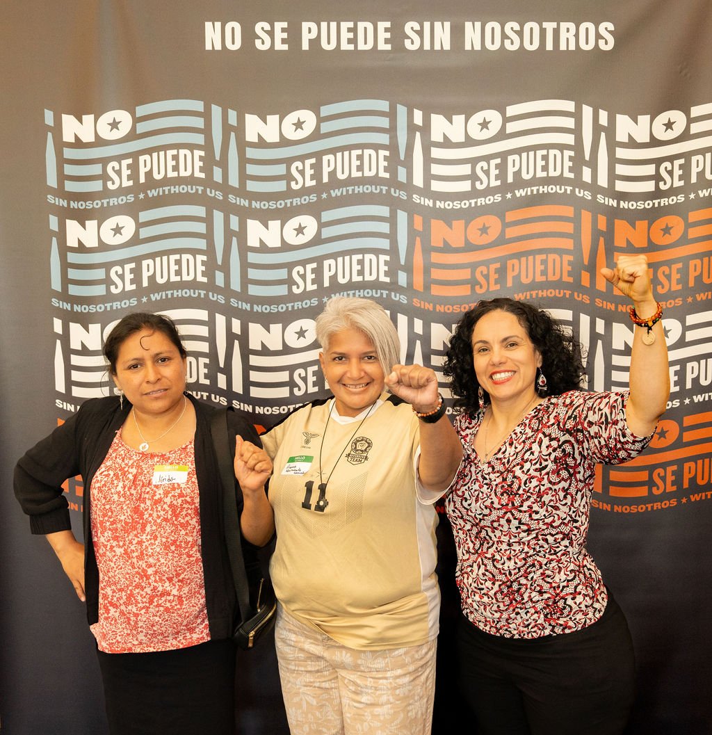 Three women standing in front of a backdrop with the words 'No Se Puede Sin Nosotros' and 'Without Us' repeated. The woman in the center is wearing a beige sports jersey with the number 10 and a medal, while the women on either side are wearing patte