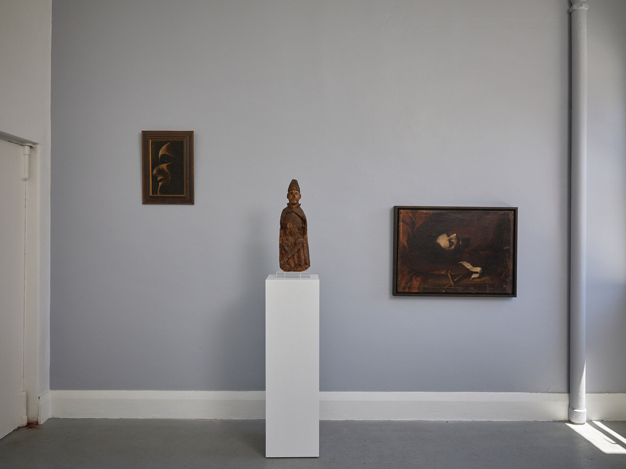Left to right: Tony Fomison Clown 1975 oil on hessian on board 365 x 220mm Romanesque Statue Late 13th - early 14th century, Iberian (probably Pyrennes) 590 x 200 x 95mm The Head of John the Baptist 17th century, Sevillian school
