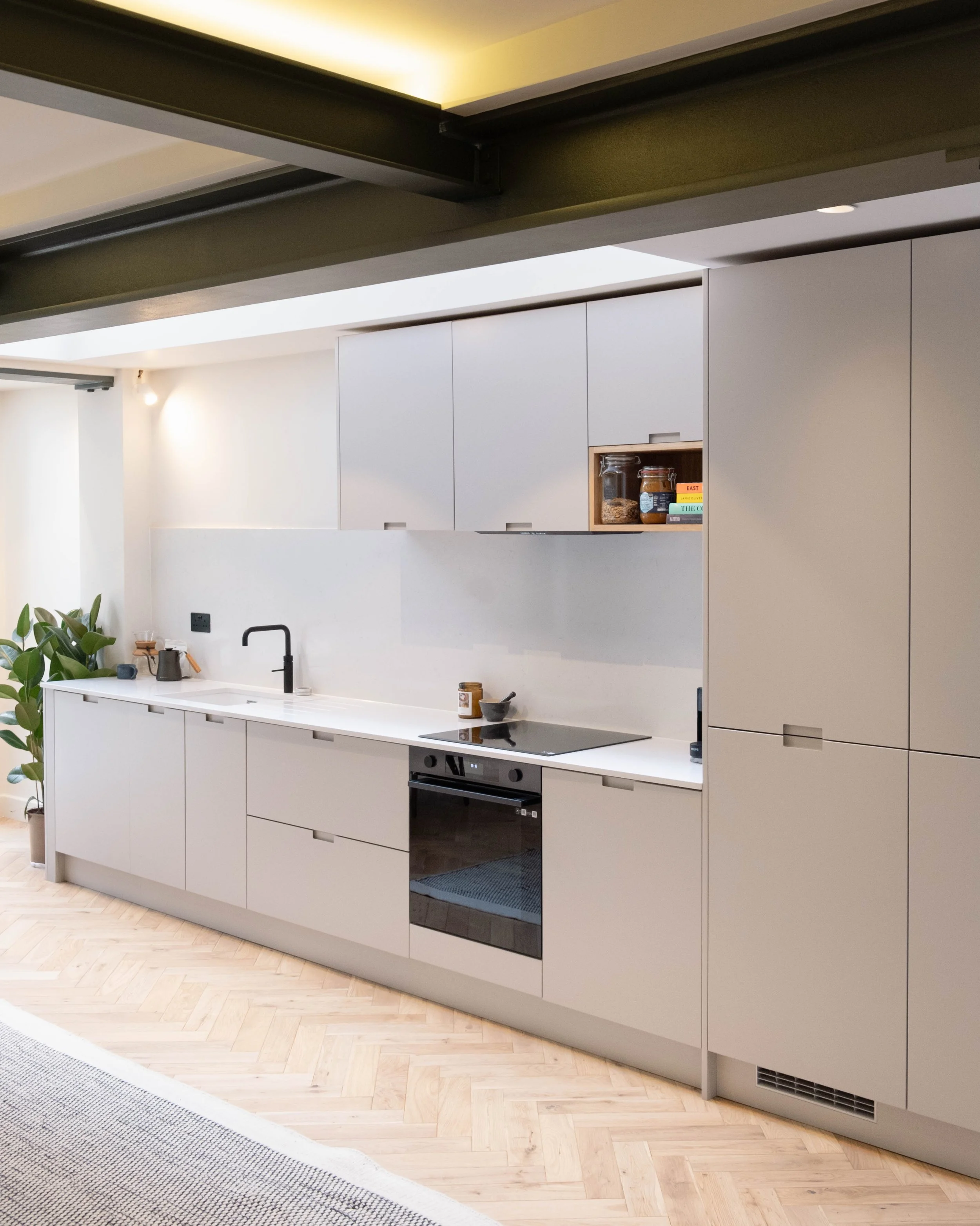 Modern kitchen with light gray cabinetry, black countertop oven, black faucet, and wooden flooring, with a potted plant on the left.