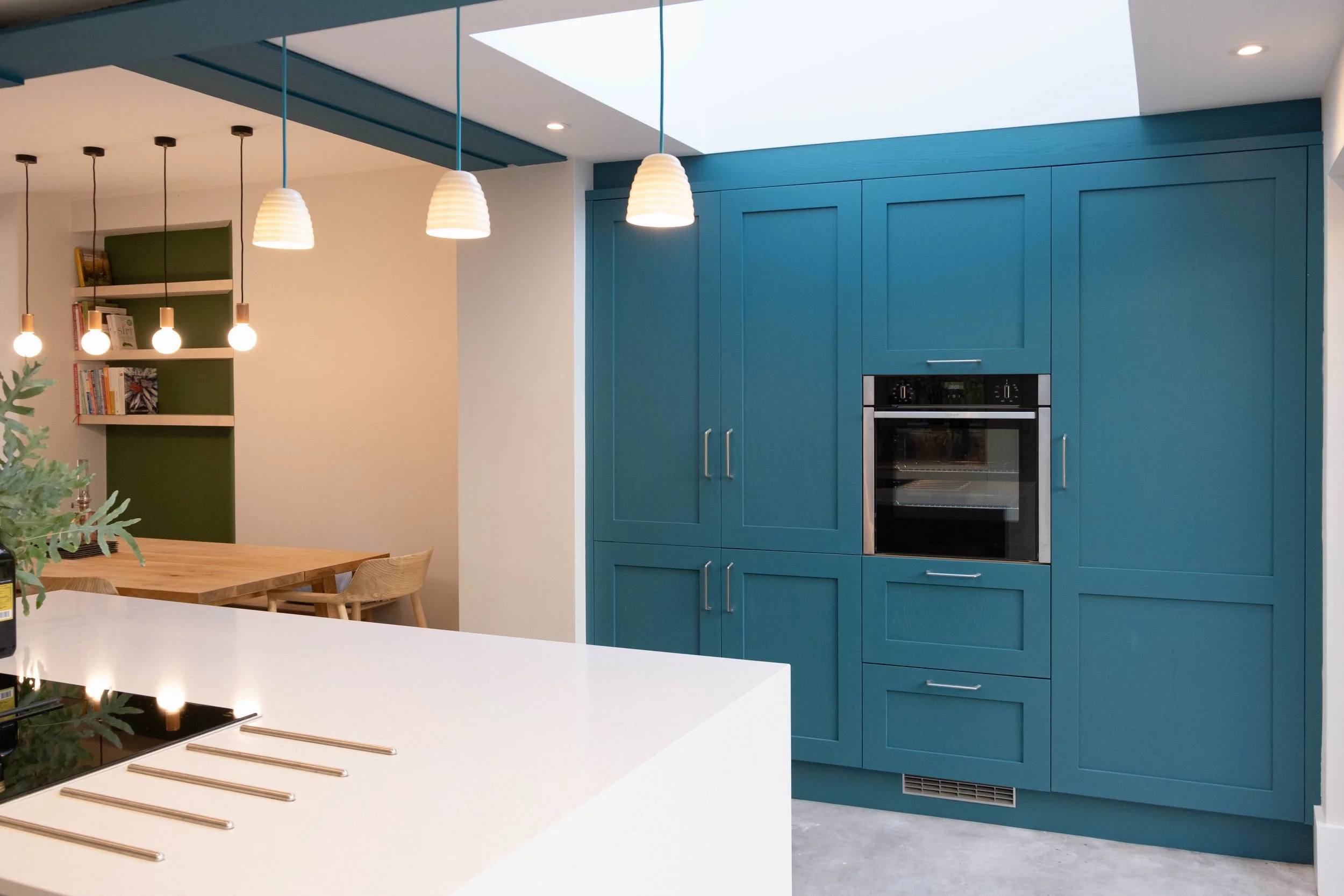 Modern kitchen with blue cabinets, built-in oven, white countertop, and pendant lights.