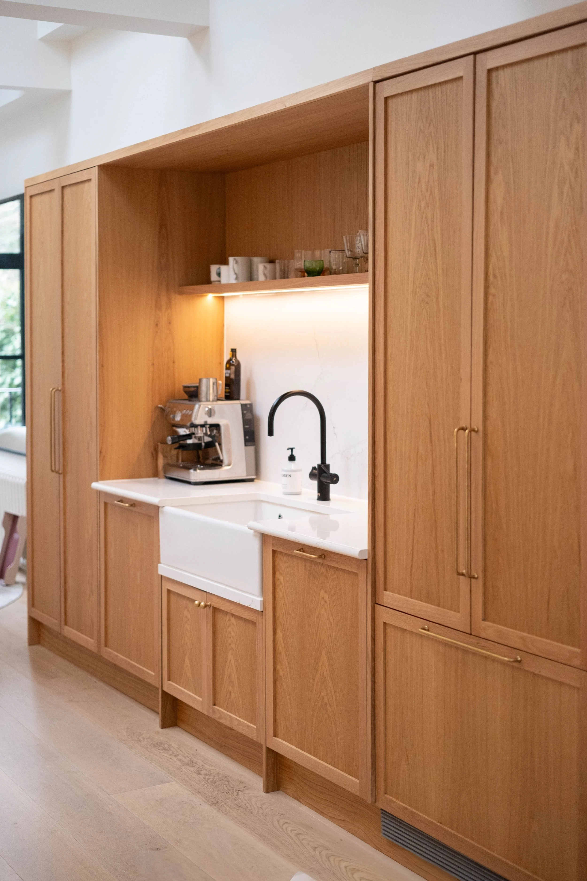 Wooden kitchen cabinets with a white farmhouse sink, a black faucet, and a coffee machine on the countertop.