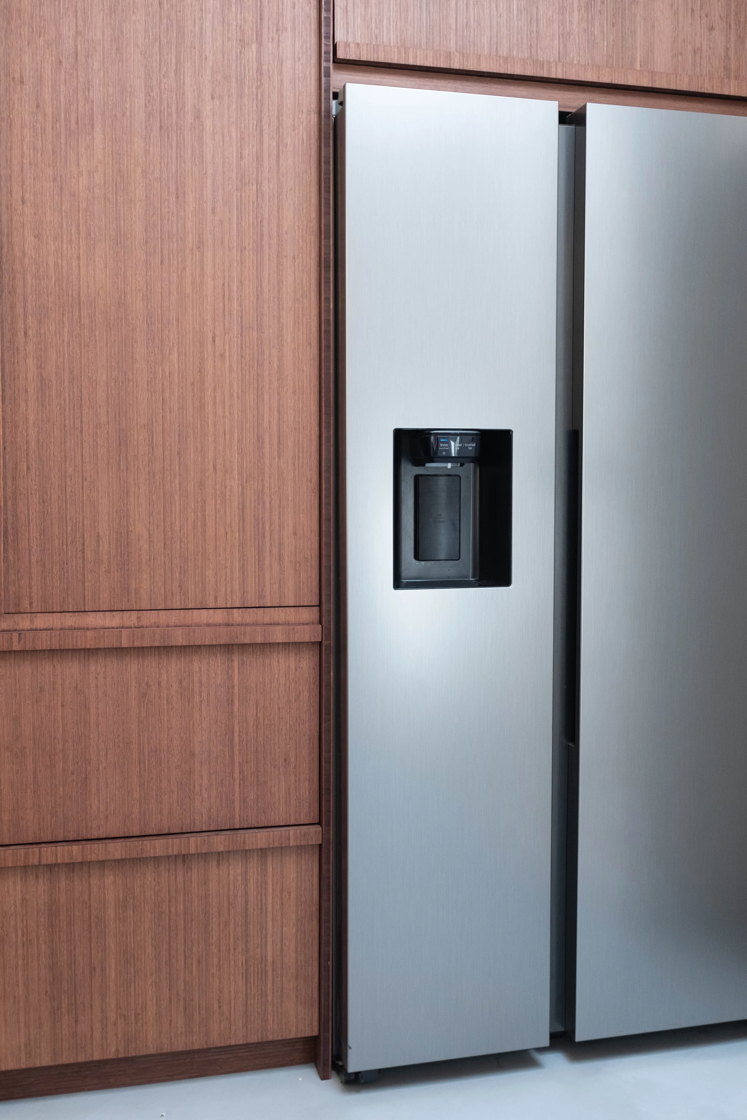 Refrigerator placed next to wooden cabinets in a modern kitchen setting.