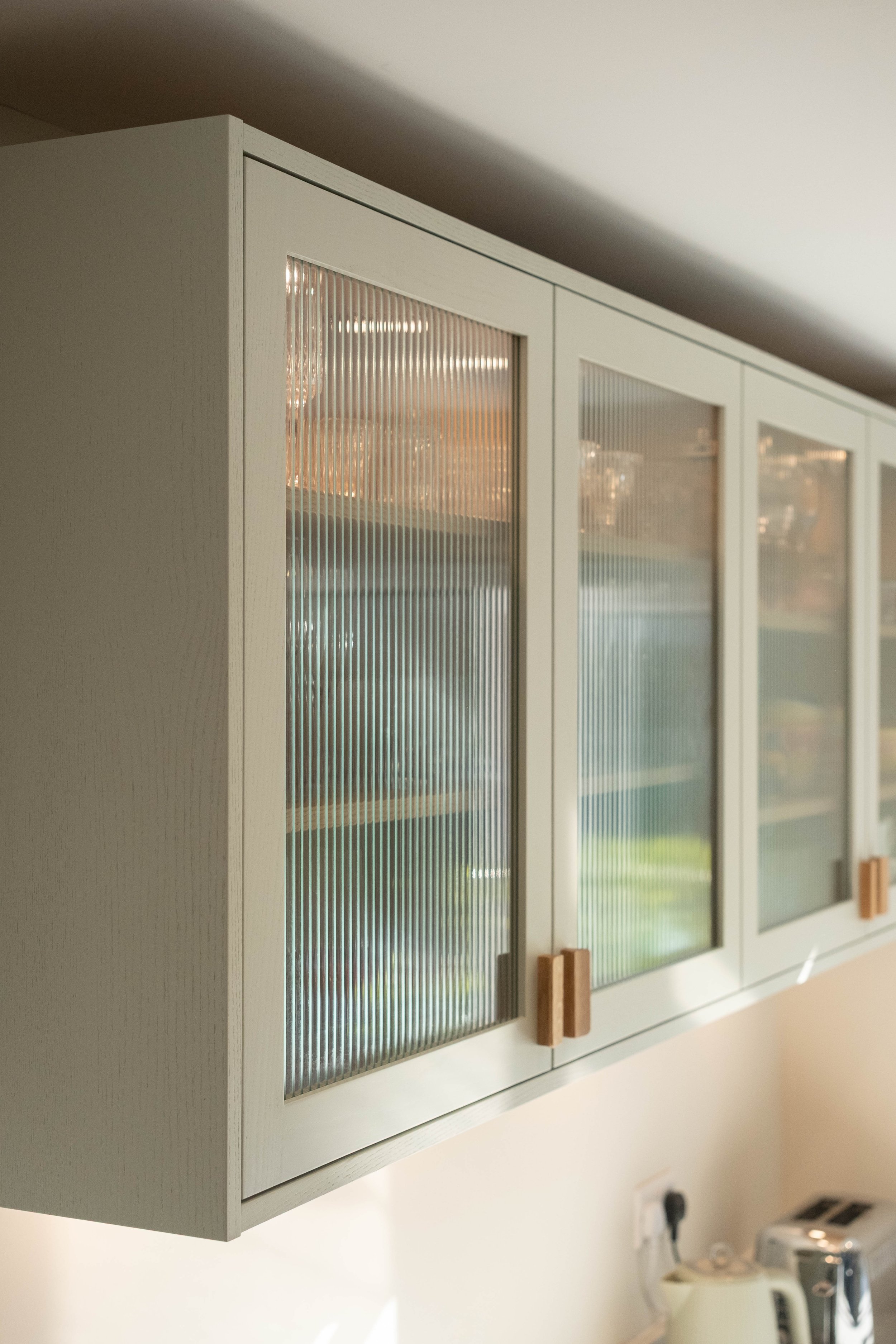 White kitchen cabinet with glass-paneled doors and wooden handles, mounted on a wall.
