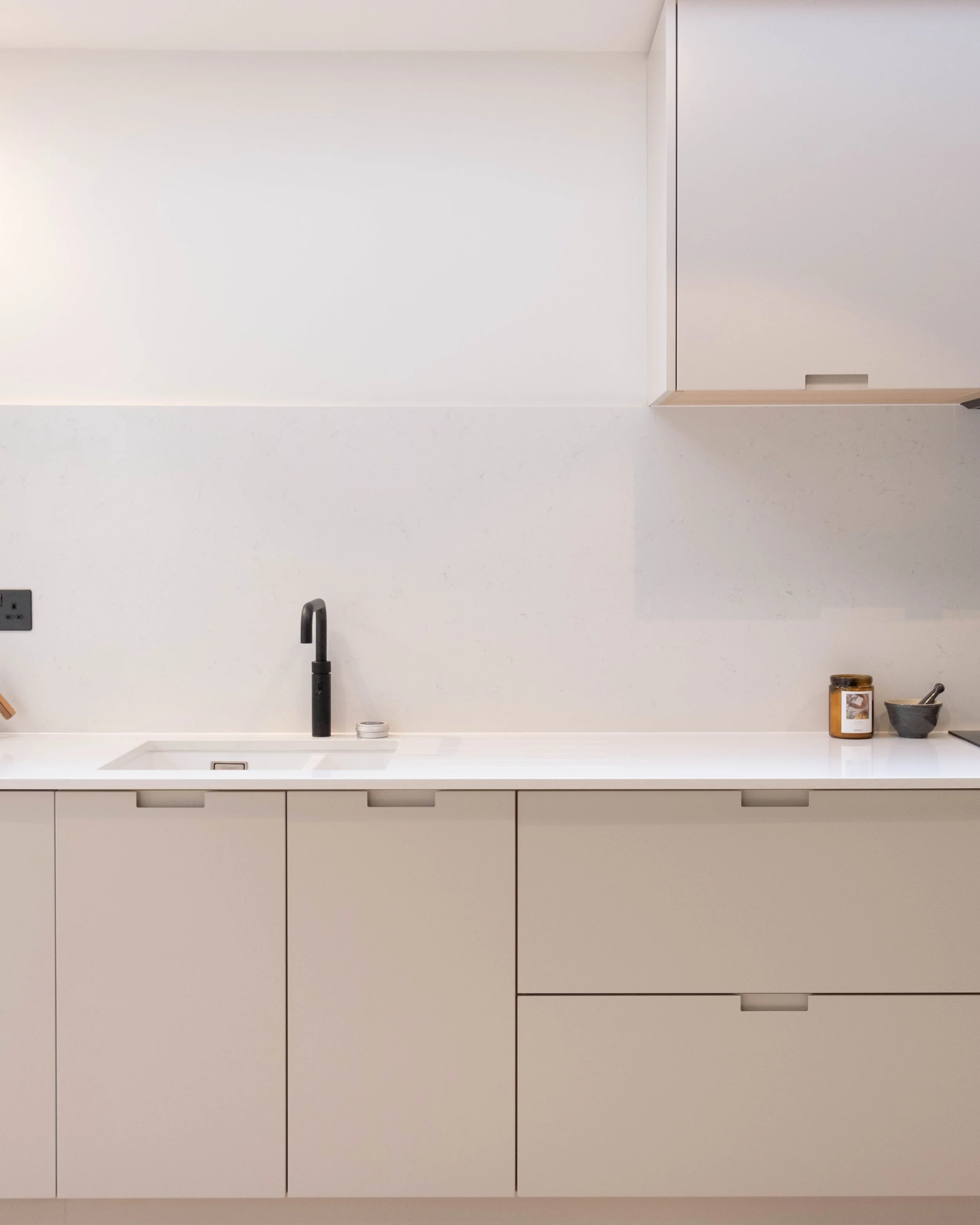 Minimalist kitchen with white cabinetry, black faucet, and a few items on the countertop including a jar, spoon, and small container.