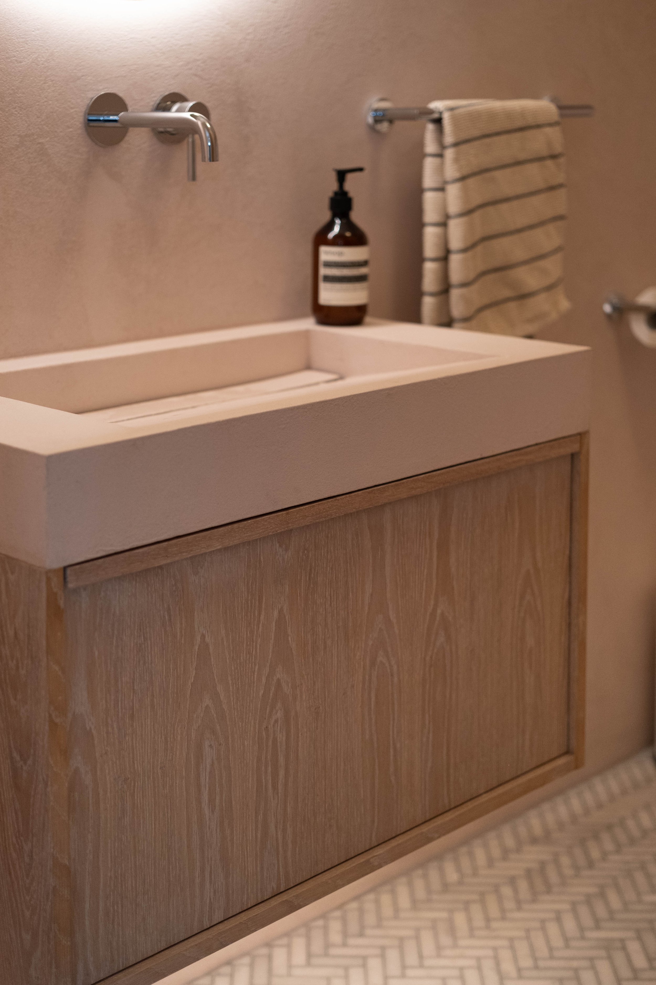Bathroom sink with a bottle of soap, a striped towel on a towel bar, and a wooden cabinet beneath the sink.