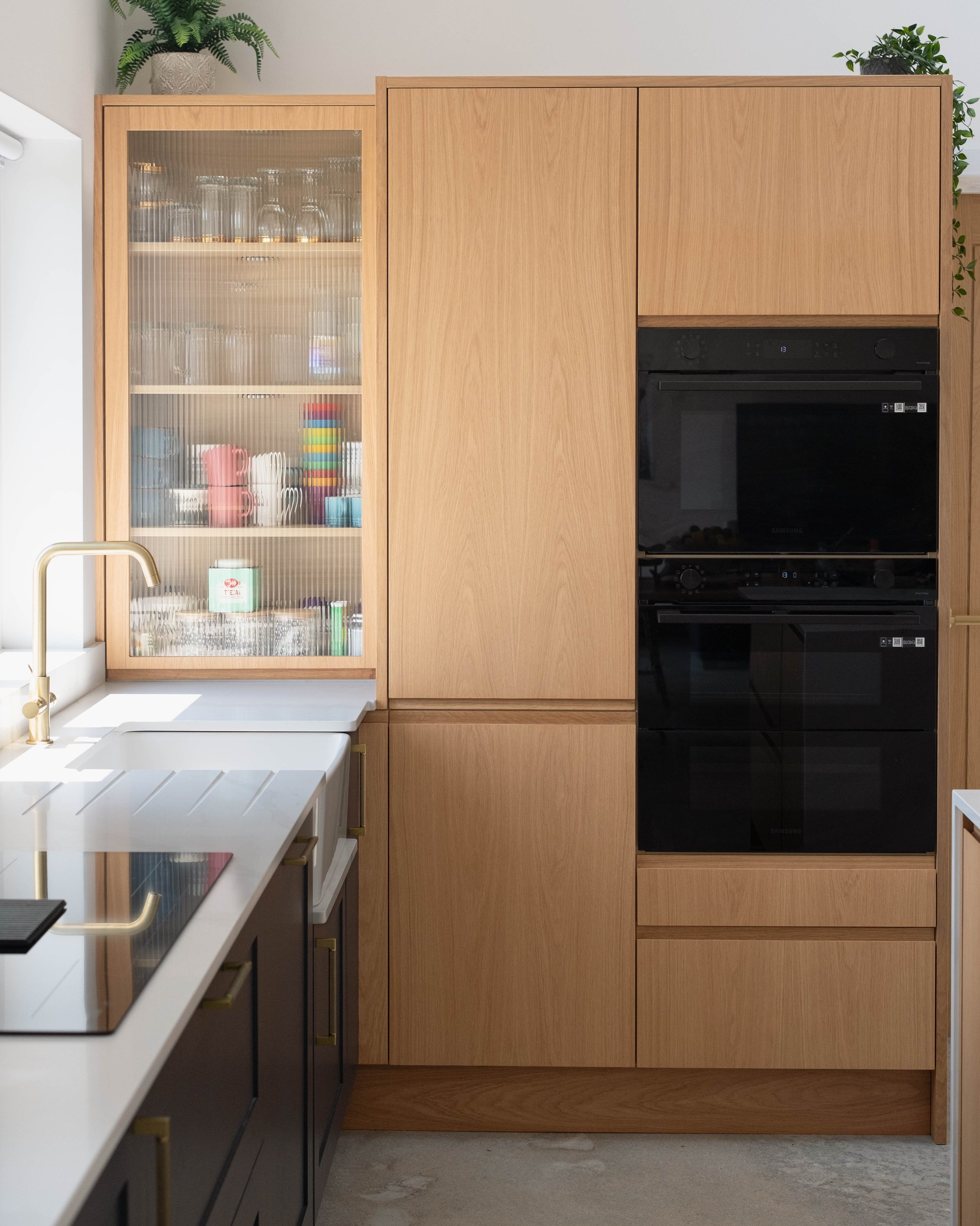 A kitchen with wooden cabinets, black appliances, and a window with a white countertop and gold faucet in the foreground.