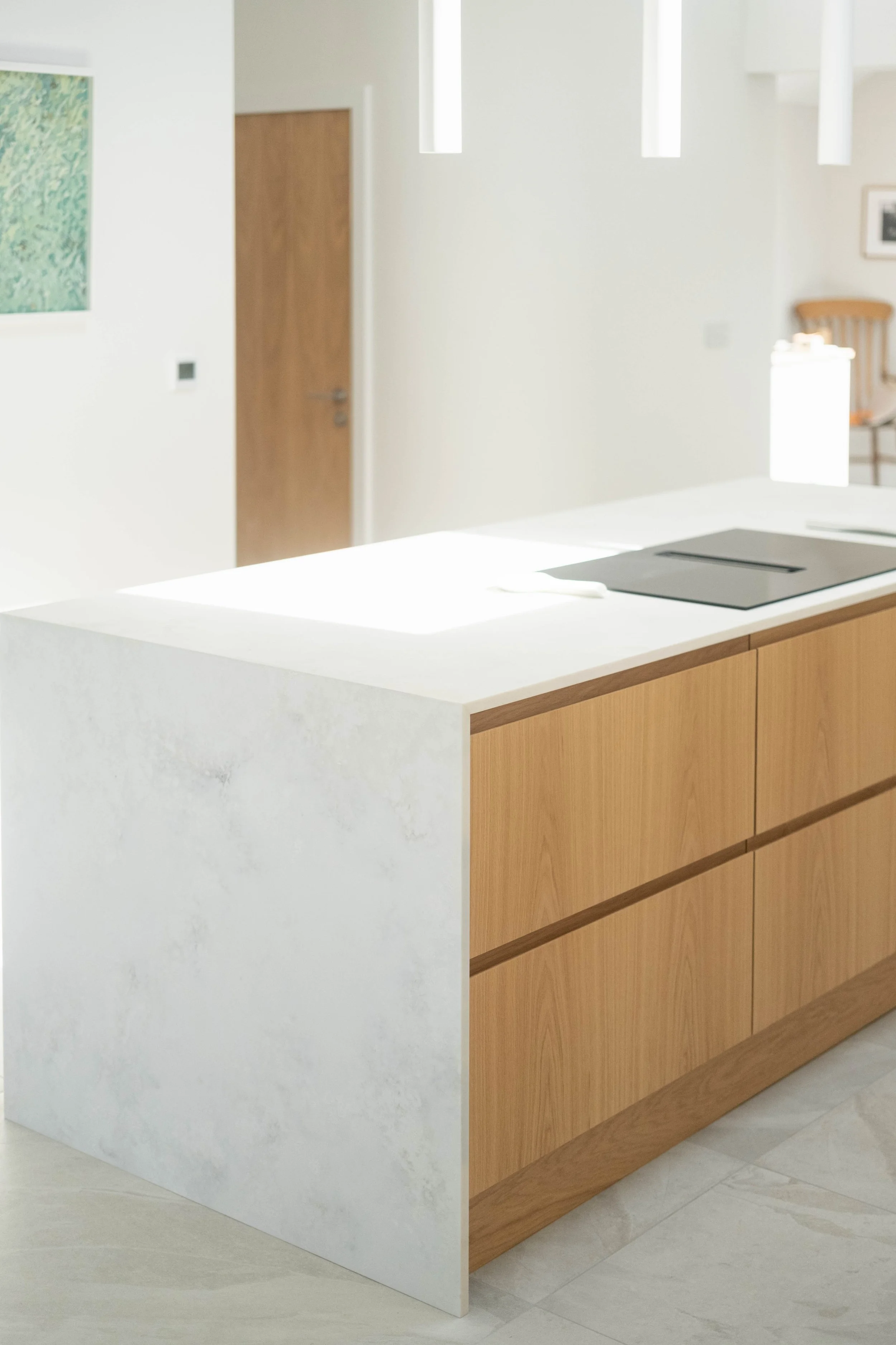 A kitchen island with a white marble top and wooden drawers, next to a white wall with a kitchen sink and appliances on the right side.