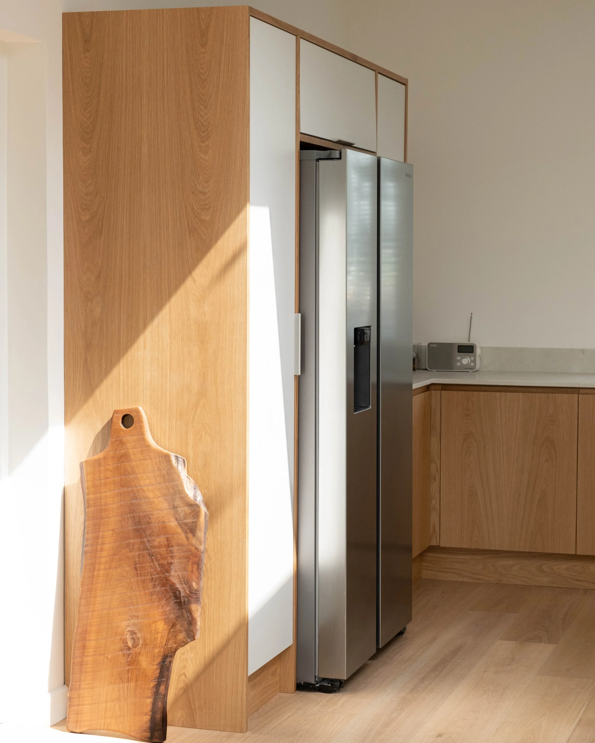 A wooden countertop with a live edge, a gray refrigerator, and a beige wall in a modern kitchen.