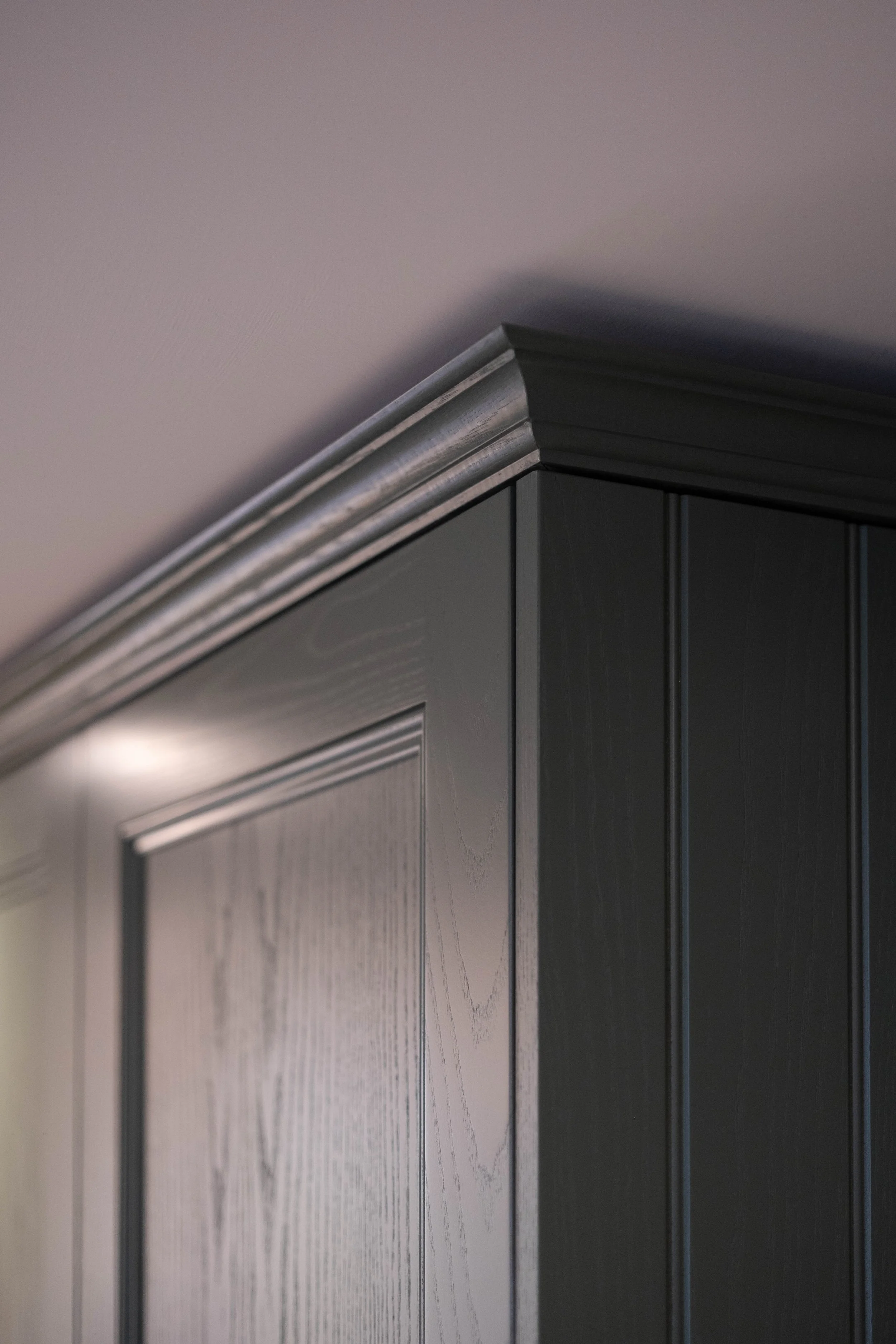 Close-up of a section of a dark gray kitchen cabinet with detailed molding on the top edge and vertical paneling on the door.