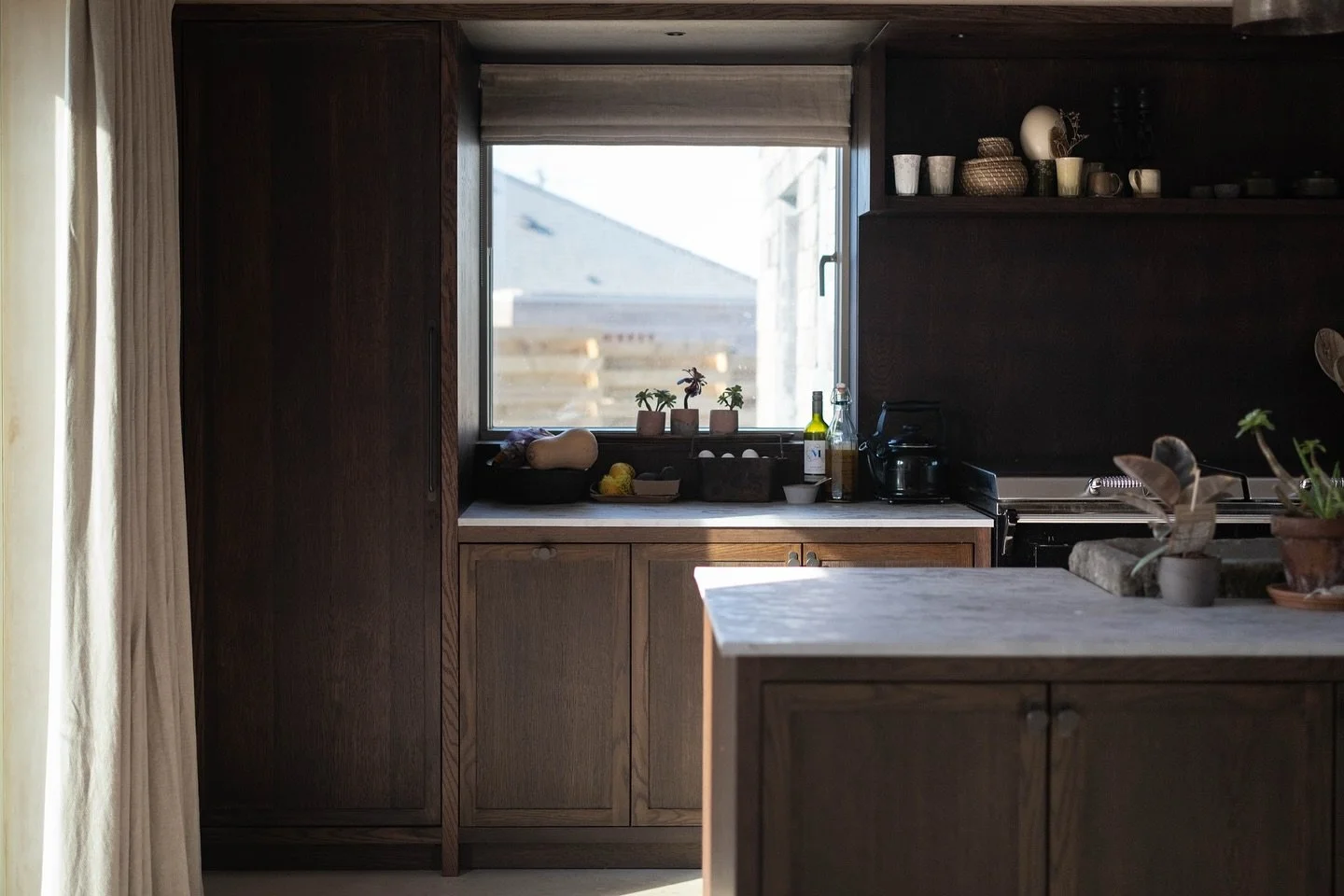 A dark stained oak, 40mm slim shaker kitchen. 

Each section is framed with 40mm panelling to keep continuity between the doors and panels. We took this panelling into the window reveal, under the bulkhead, and clad the entrance into the kitchen area