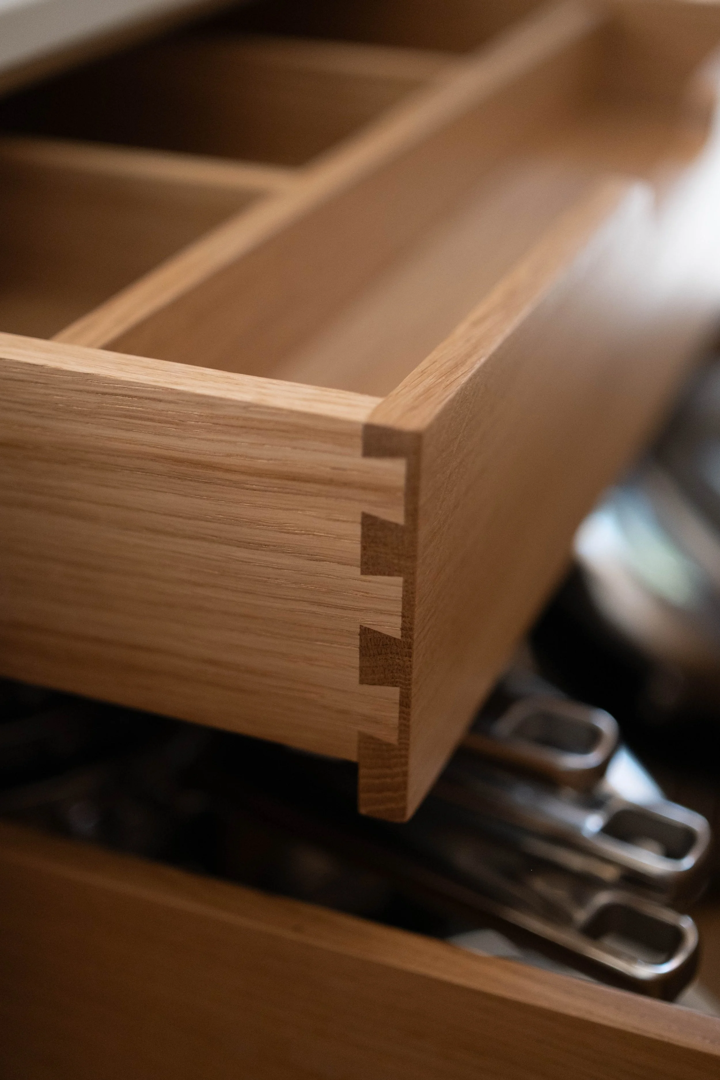 Close-up of a wooden storage drawer or box with dividers, partially open and revealing metal utensils inside.