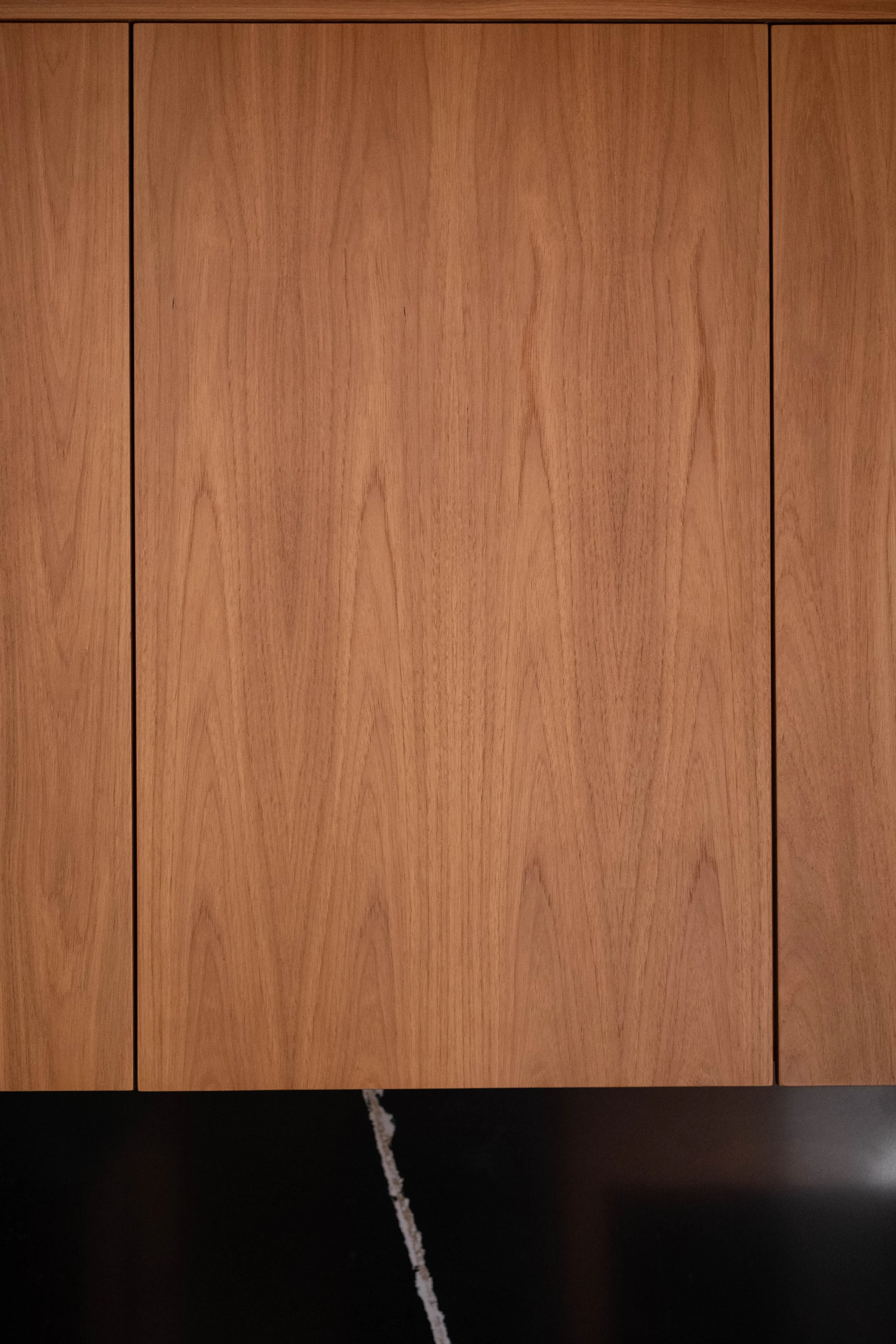 A wooden table with vertical panels and a black surface underneath, with a white line running across the surface and a small white object near the bottom edge.