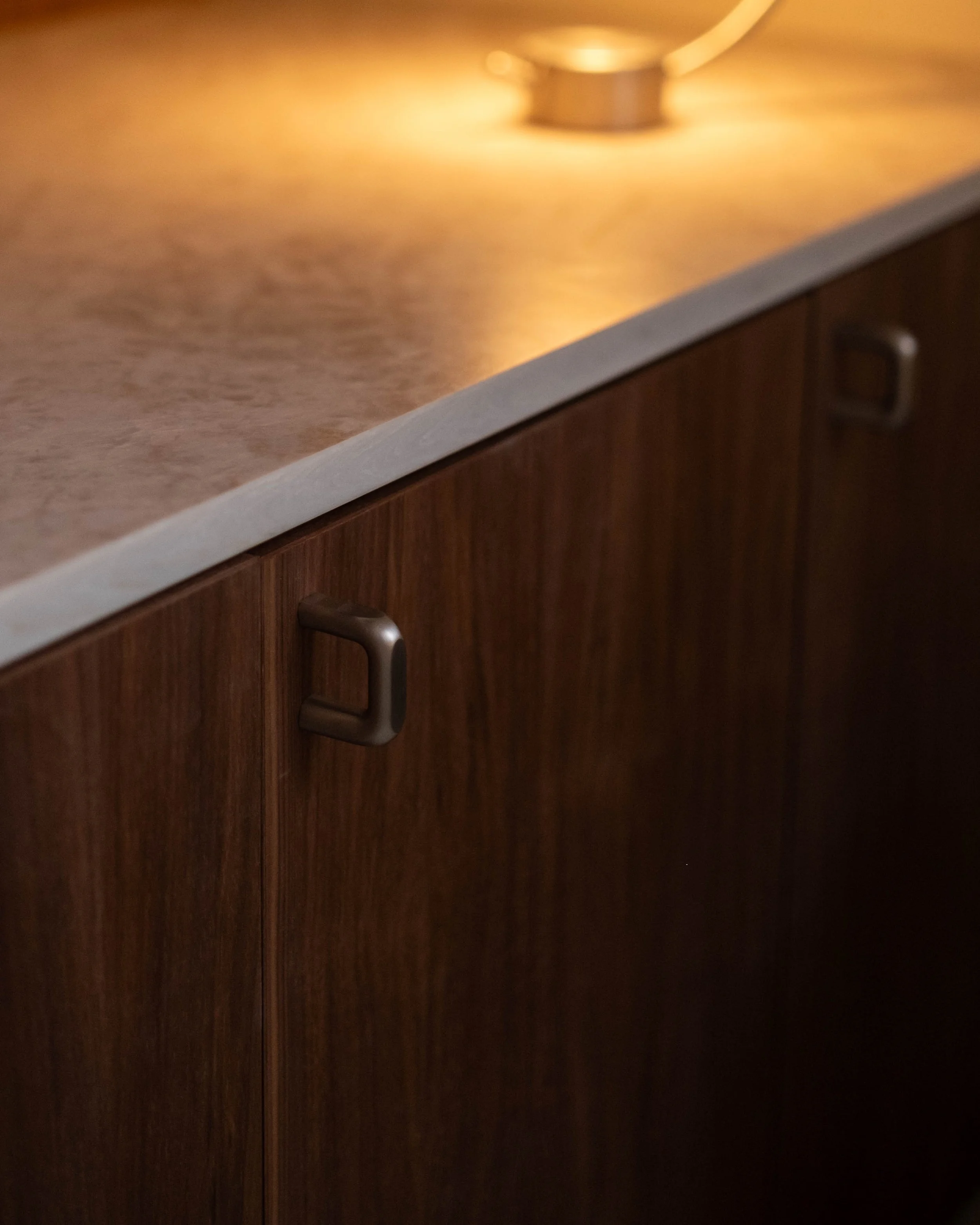Close-up of a cabinet with a brass handle and a circular silver object on a beige countertop.