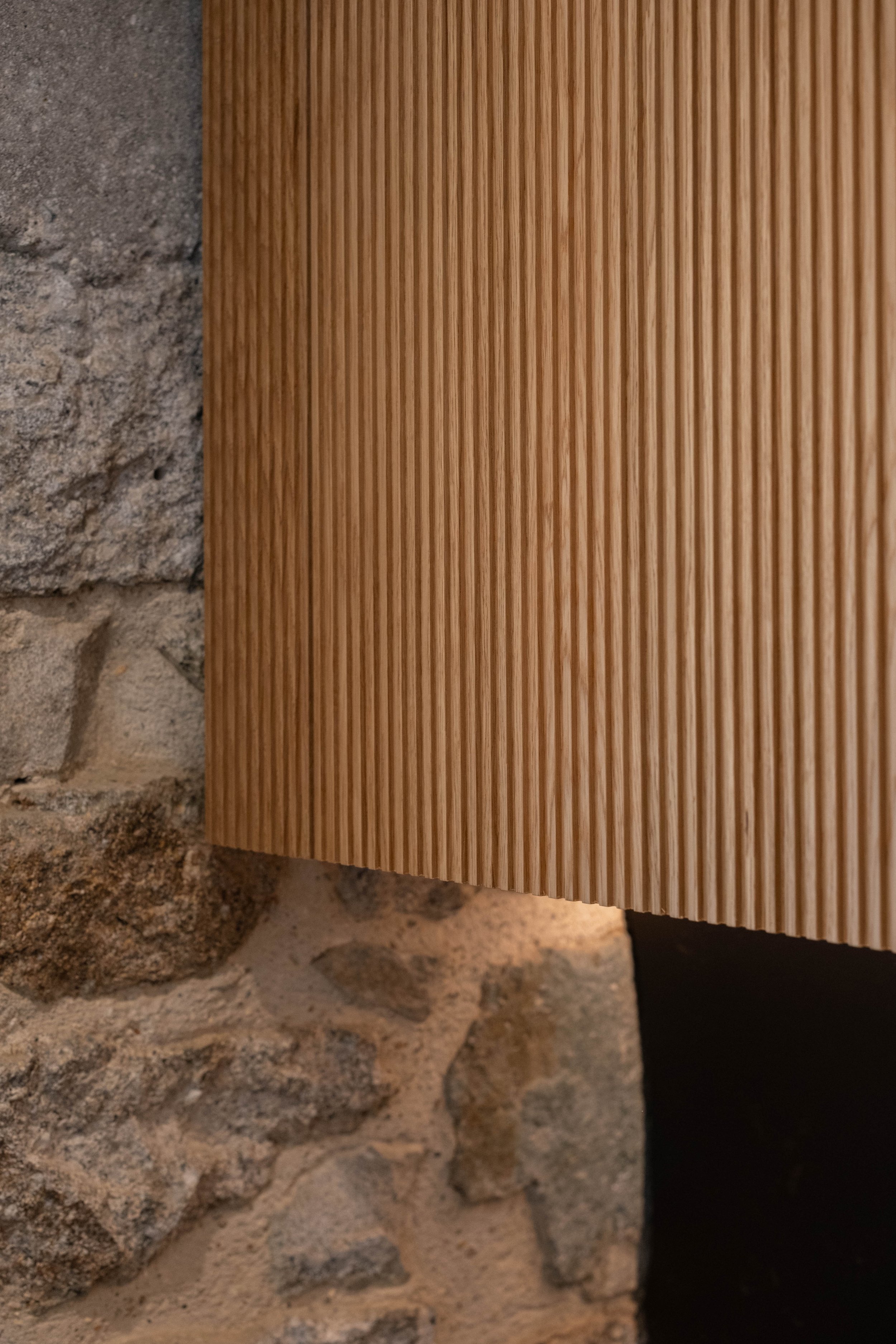 Close-up of a wooden panel with narrow, vertical grooves mounted on a rough brick wall.