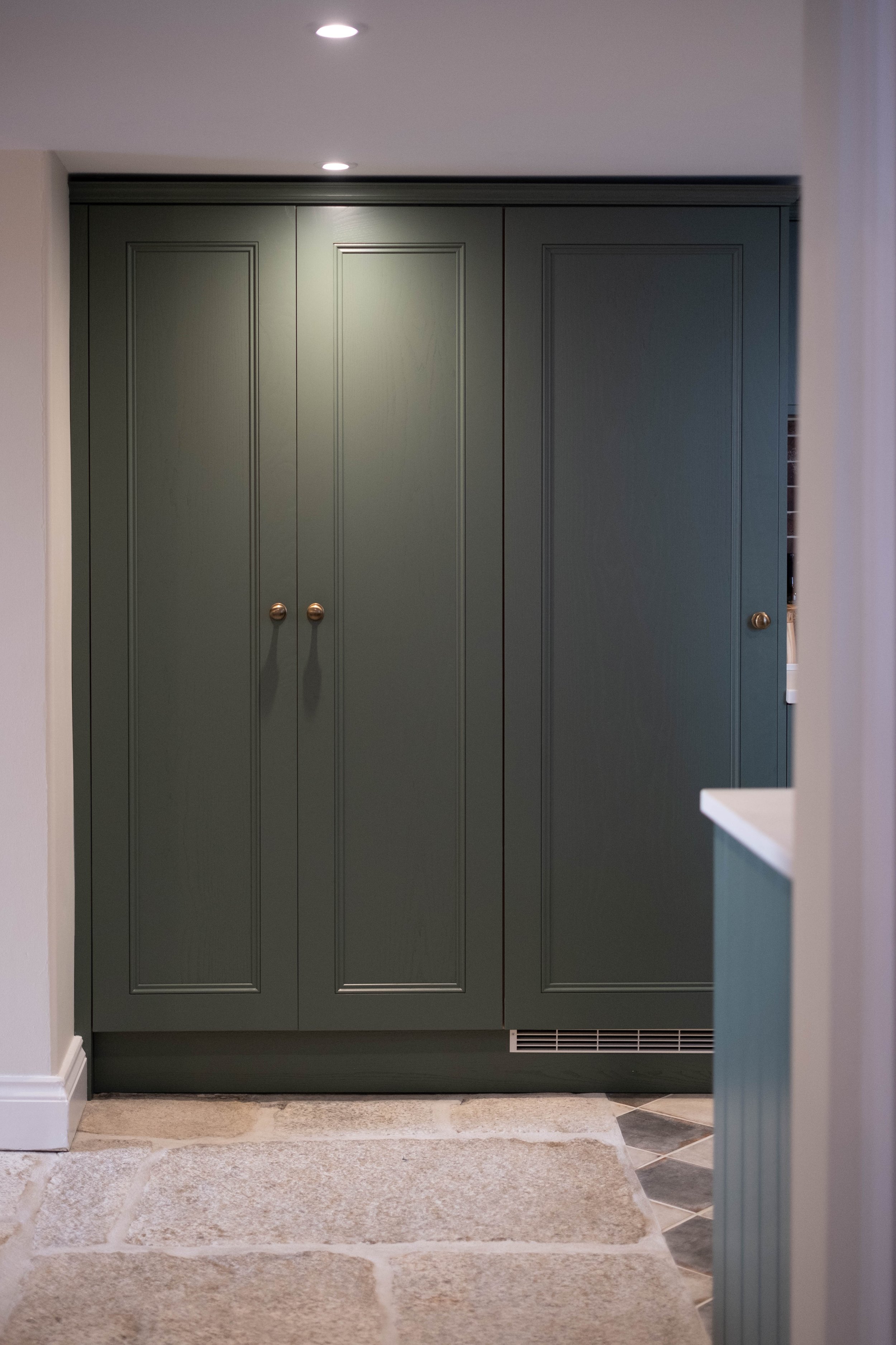 A green double-door cabinet in a room with beige and tiled flooring, framed by white walls and partially visible kitchen or living area to the right.