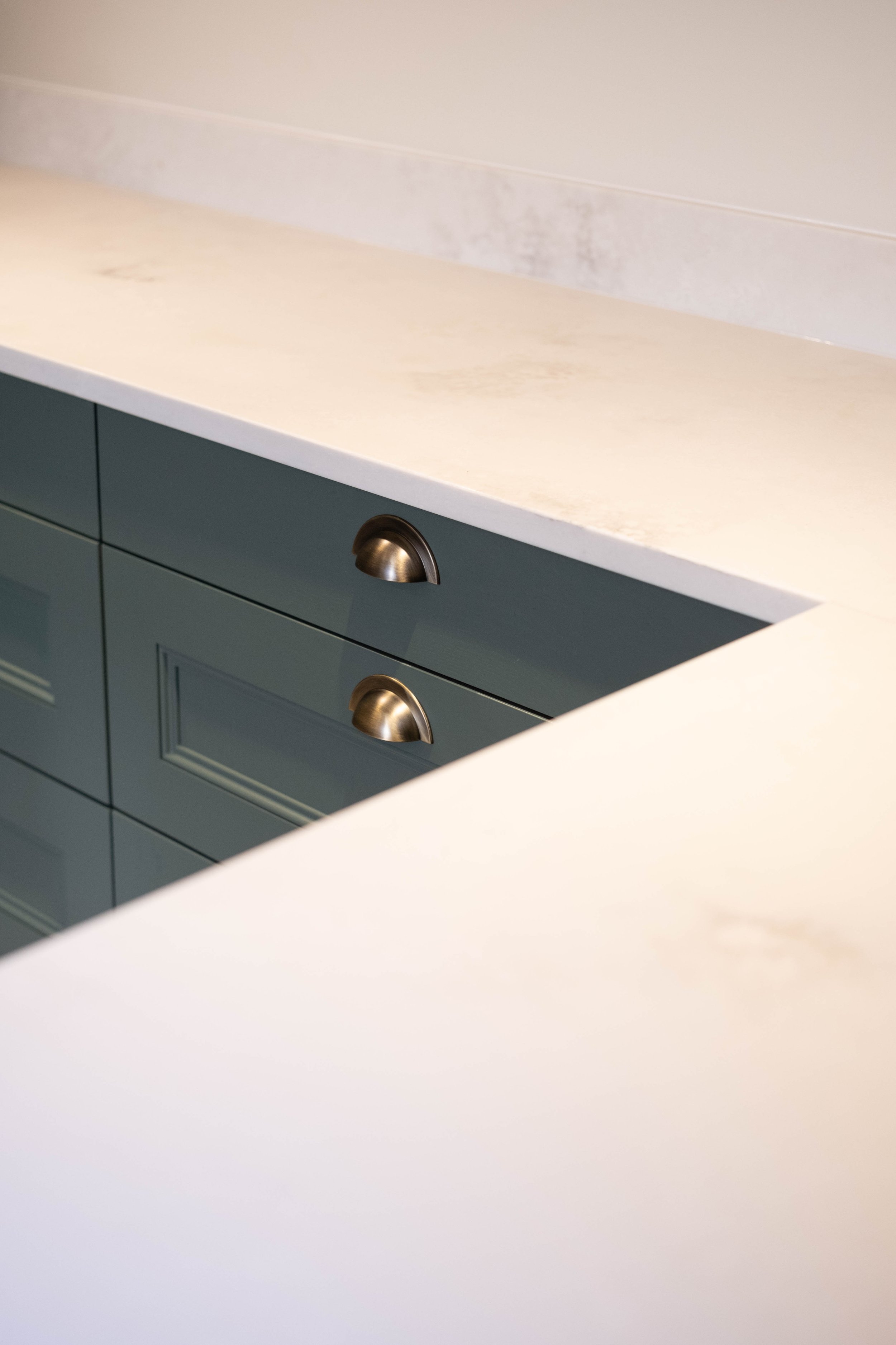 Close-up of a modern kitchen cabinet with wooden drawers, bronze handles, and a white countertop.
