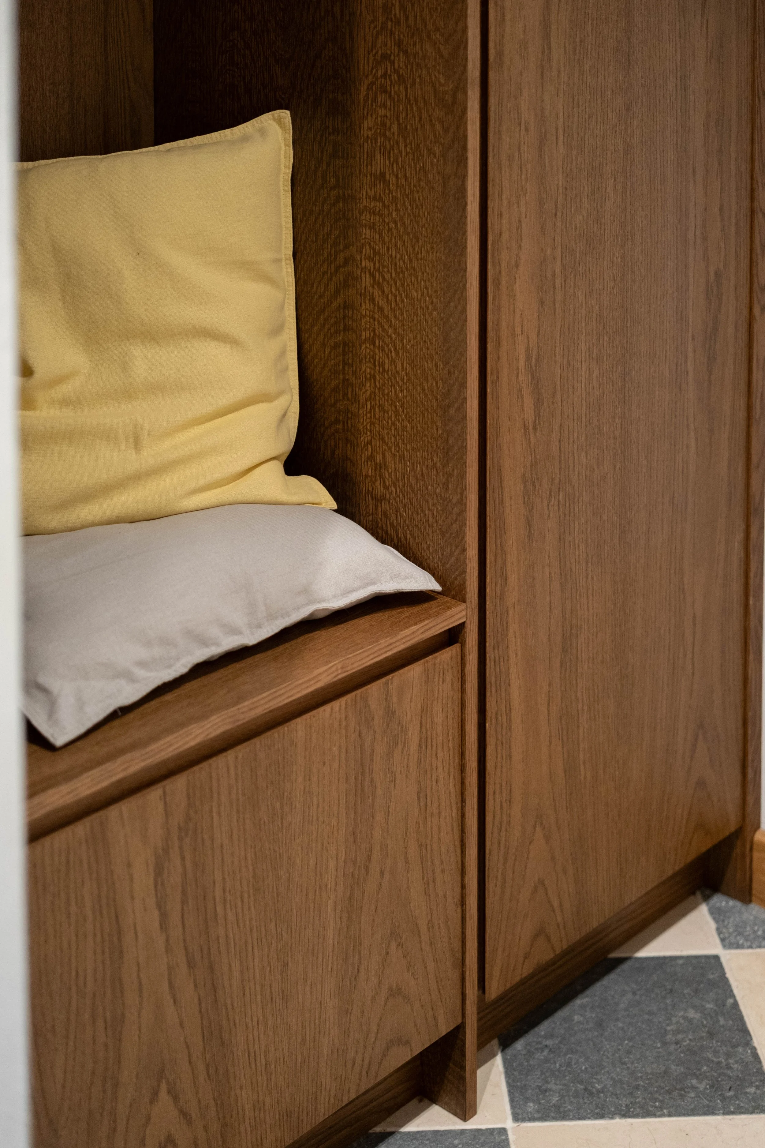 Close-up of a wooden bed headboard with a light-colored pillow and a white bed sheet, next to a wooden cabinet in a bedroom or hotel room.