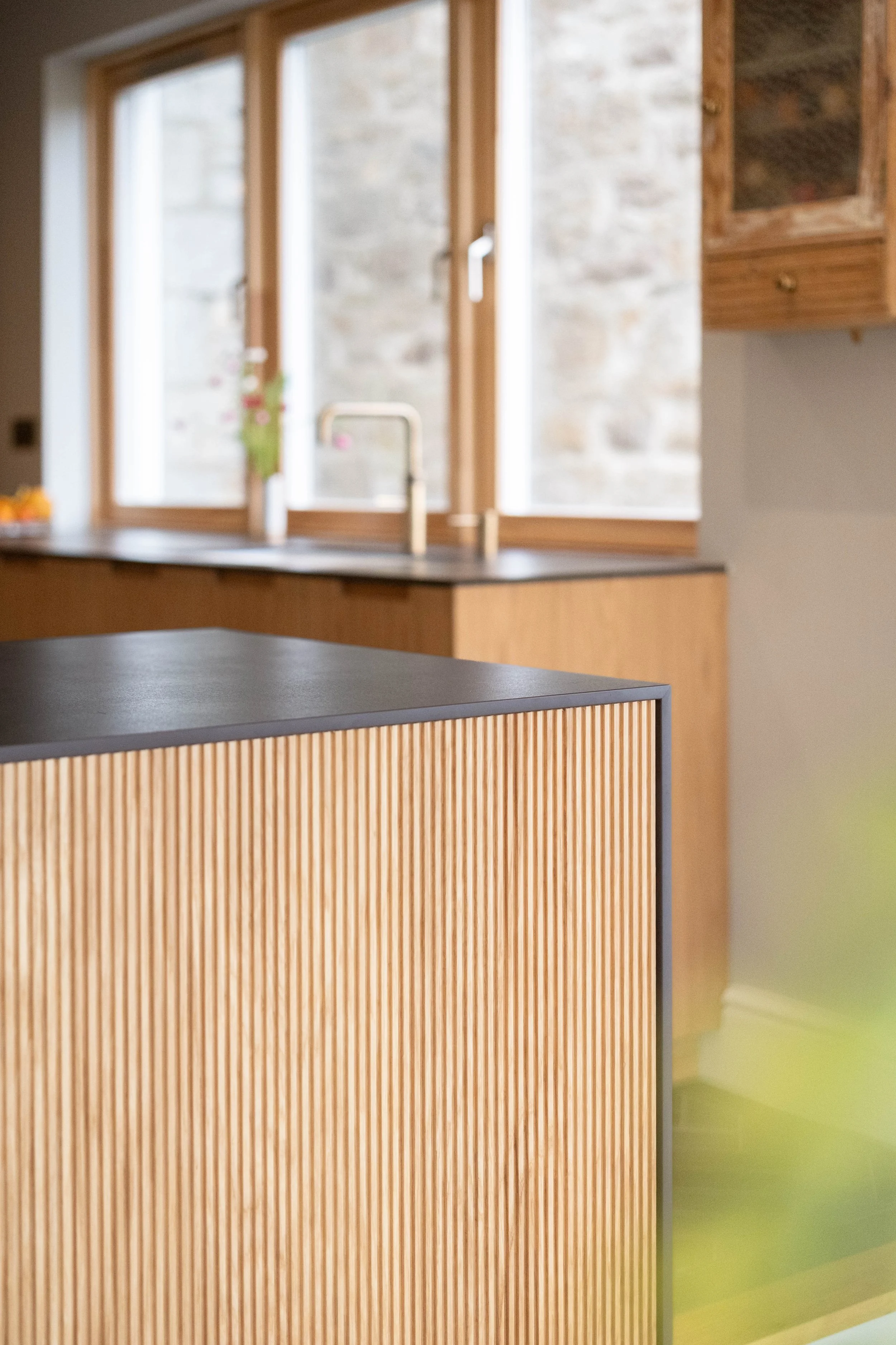 Close-up of a wooden kitchen island with a dark countertop in front of a window with wooden frames, and a stone wall outside.