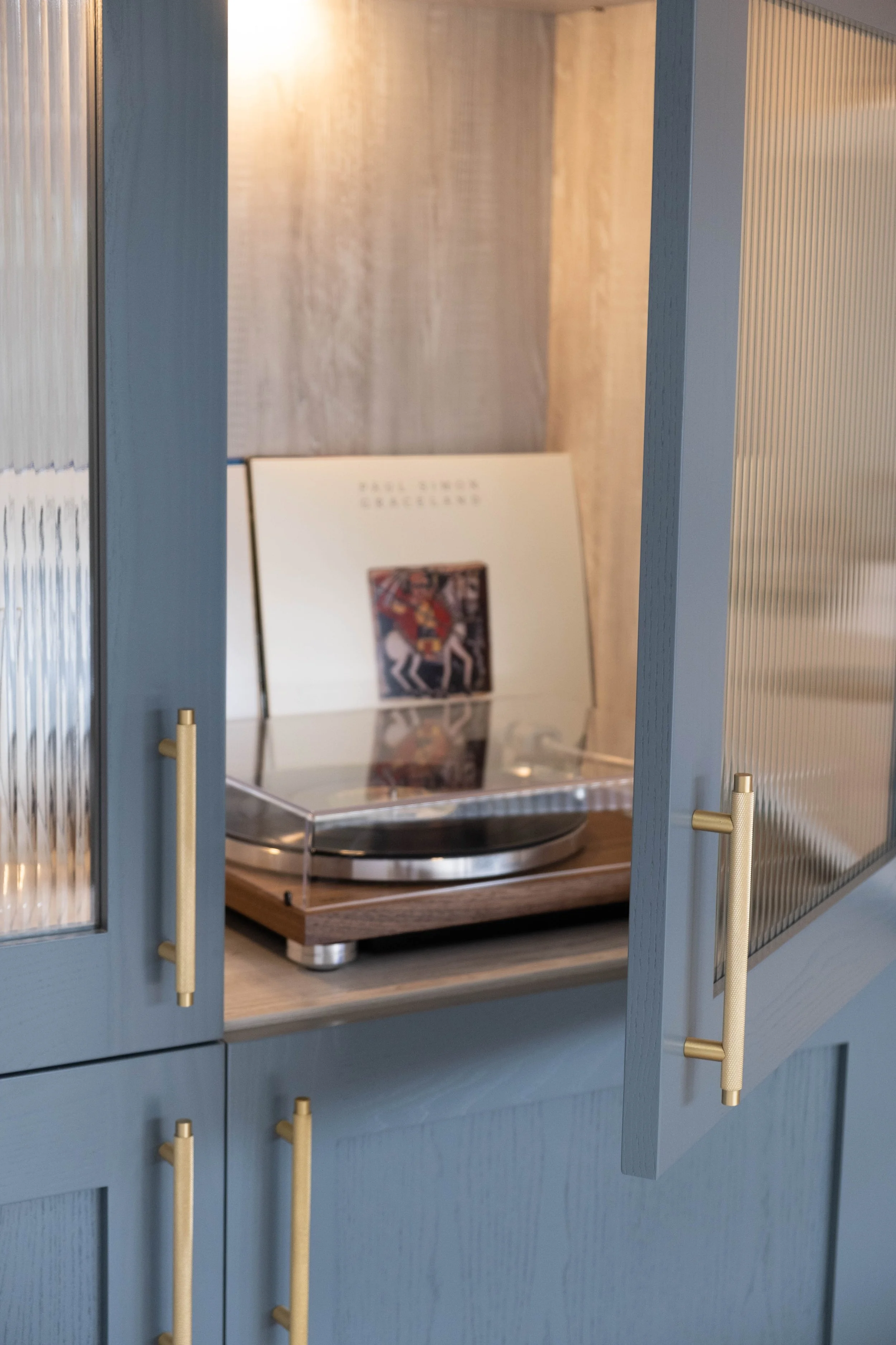 A record player on a wooden surface inside a blue cabinet with glass-paneled doors, with a book or album standing behind it.