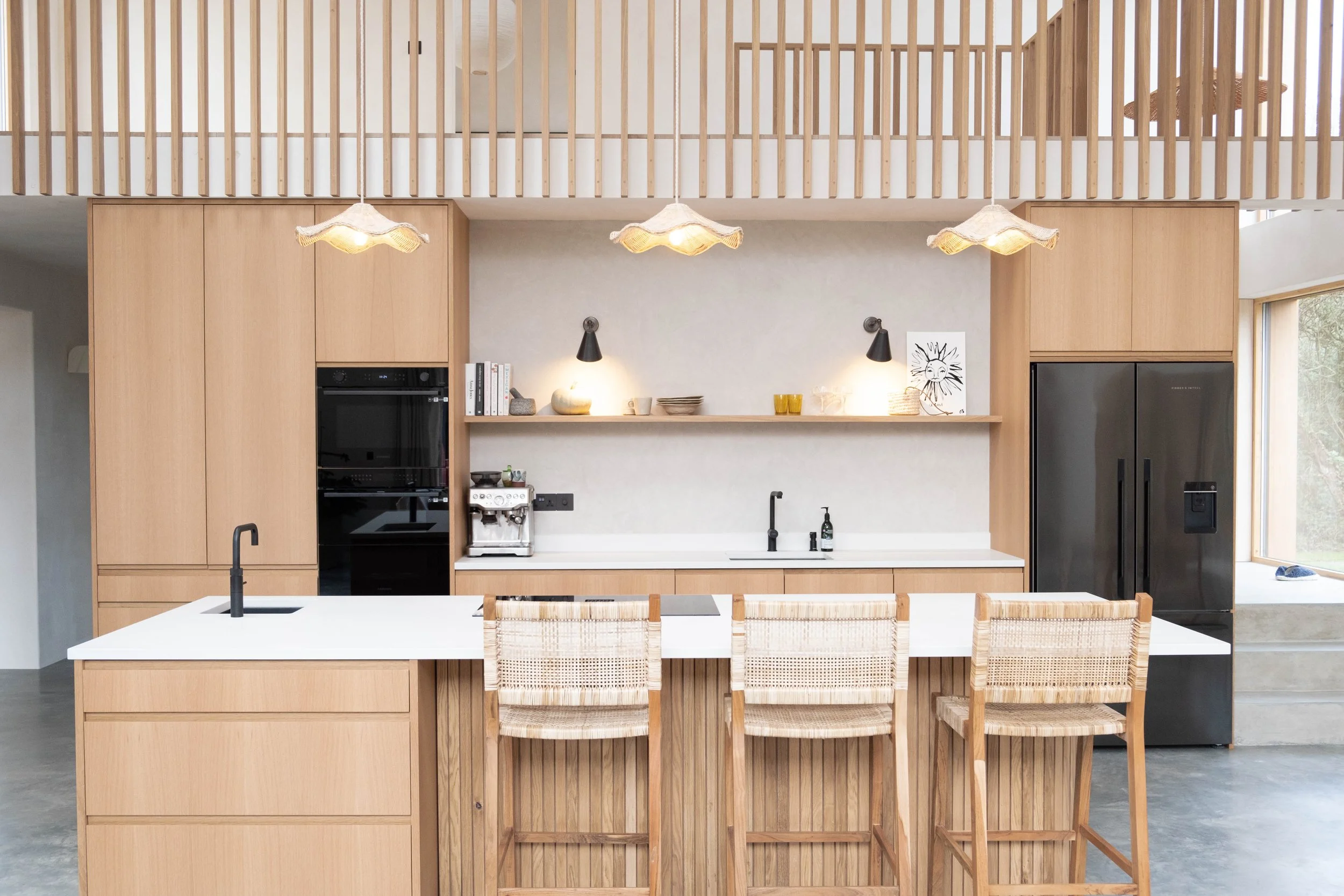 Modern kitchen with wooden cabinets, a kitchen island with a white countertop, hanging pendant lights, and a backsplash with shelf decor including books, bowls, and a drawing of a sun.