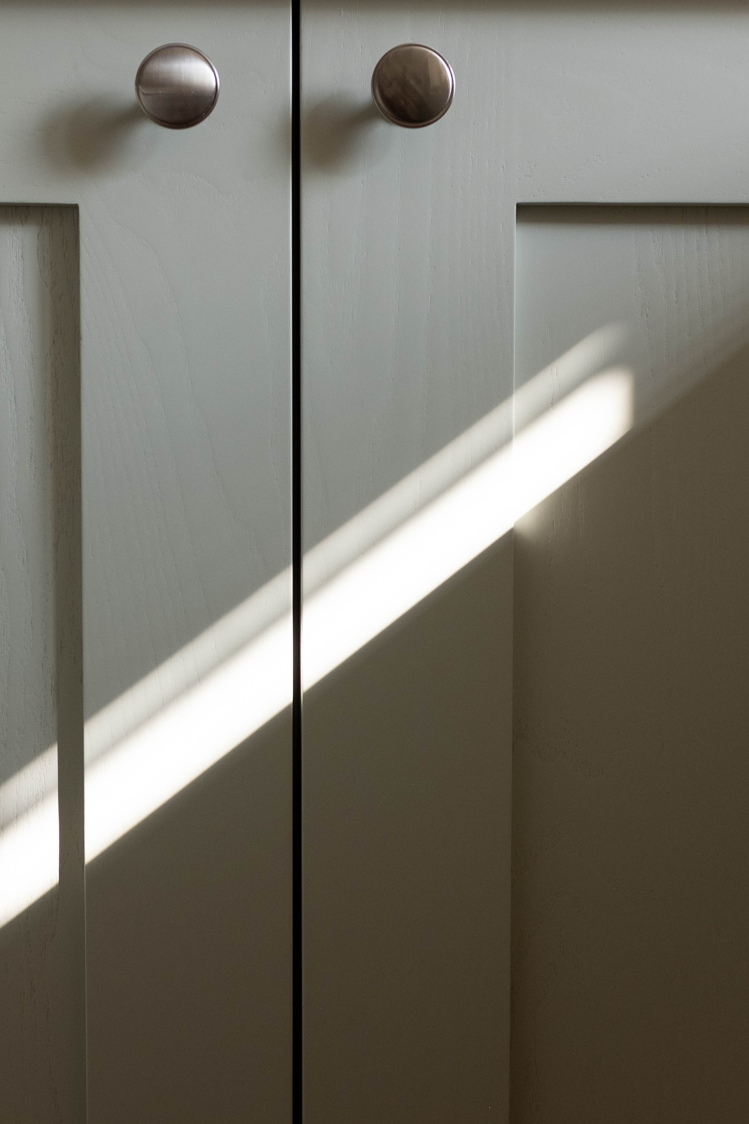 Close-up photo of white cabinet doors with round silver knobs, sunlight casting diagonal shadows on the doors.