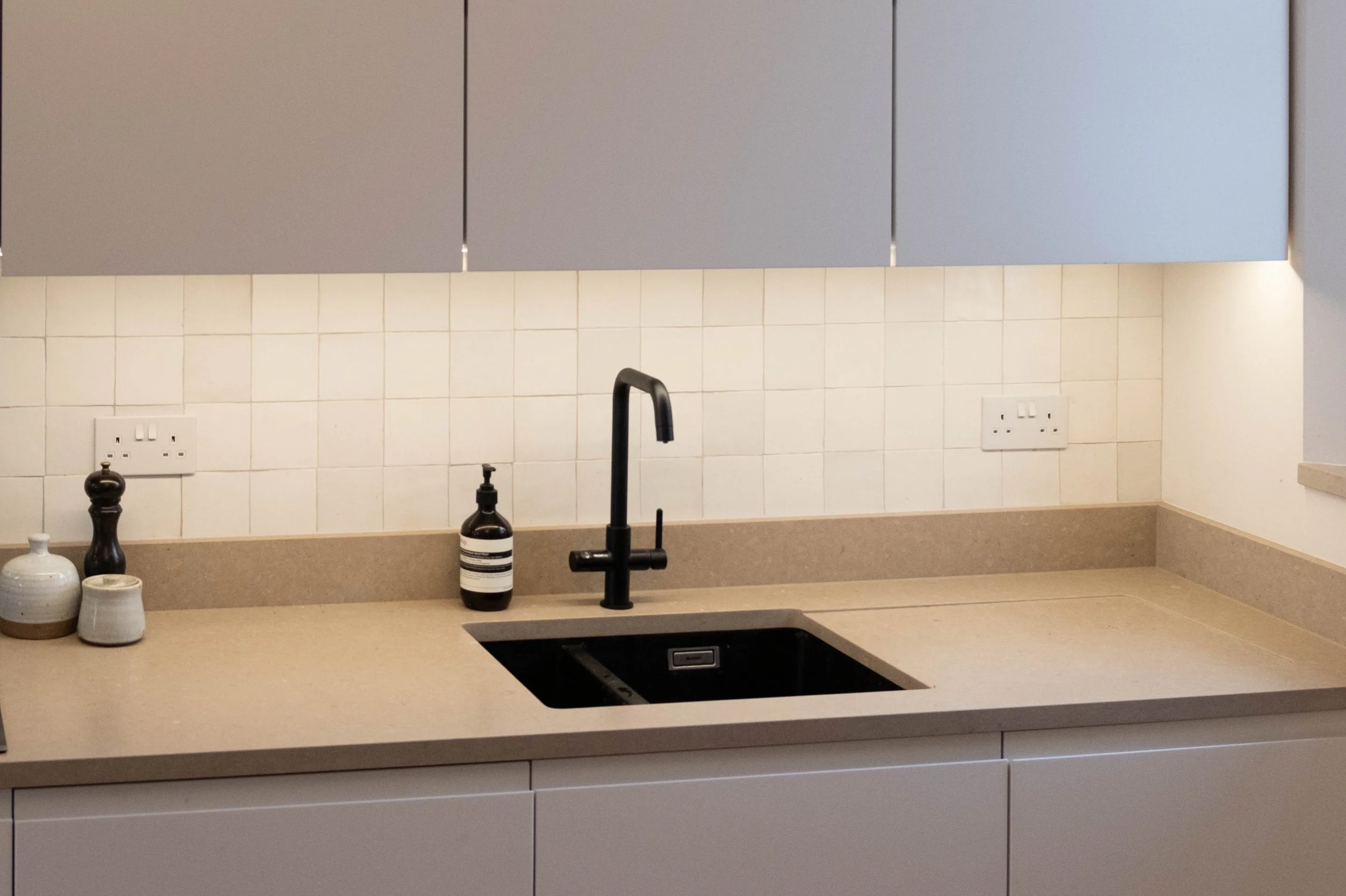 A kitchen countertop with a black faucet, a soap dispenser, and decorative vases, with white tiled backsplash and beige lower cabinets.