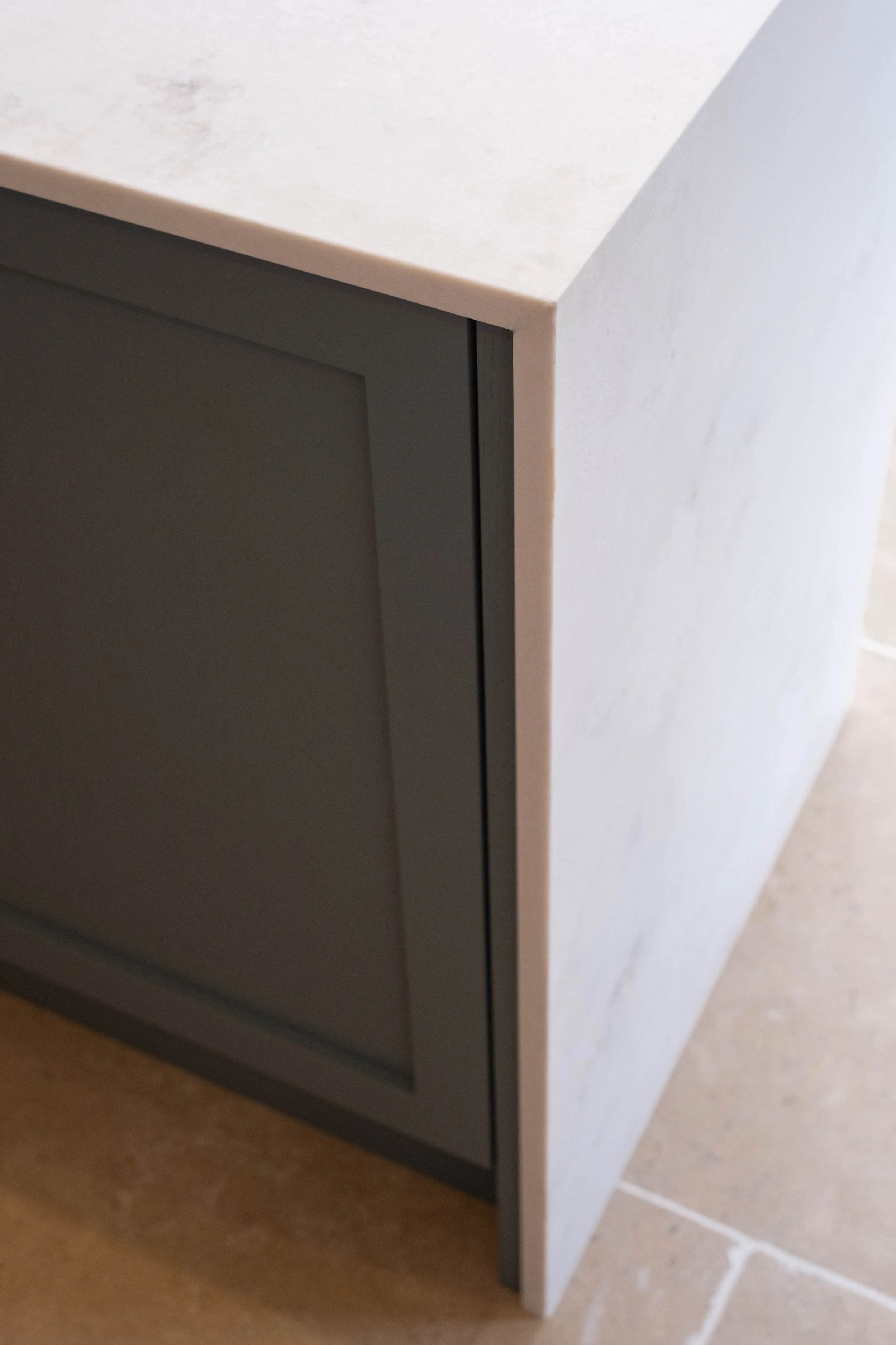 Close-up of a corner of a modern cabinet with a white marble top and a dark gray door, set against a light-colored tiled floor.