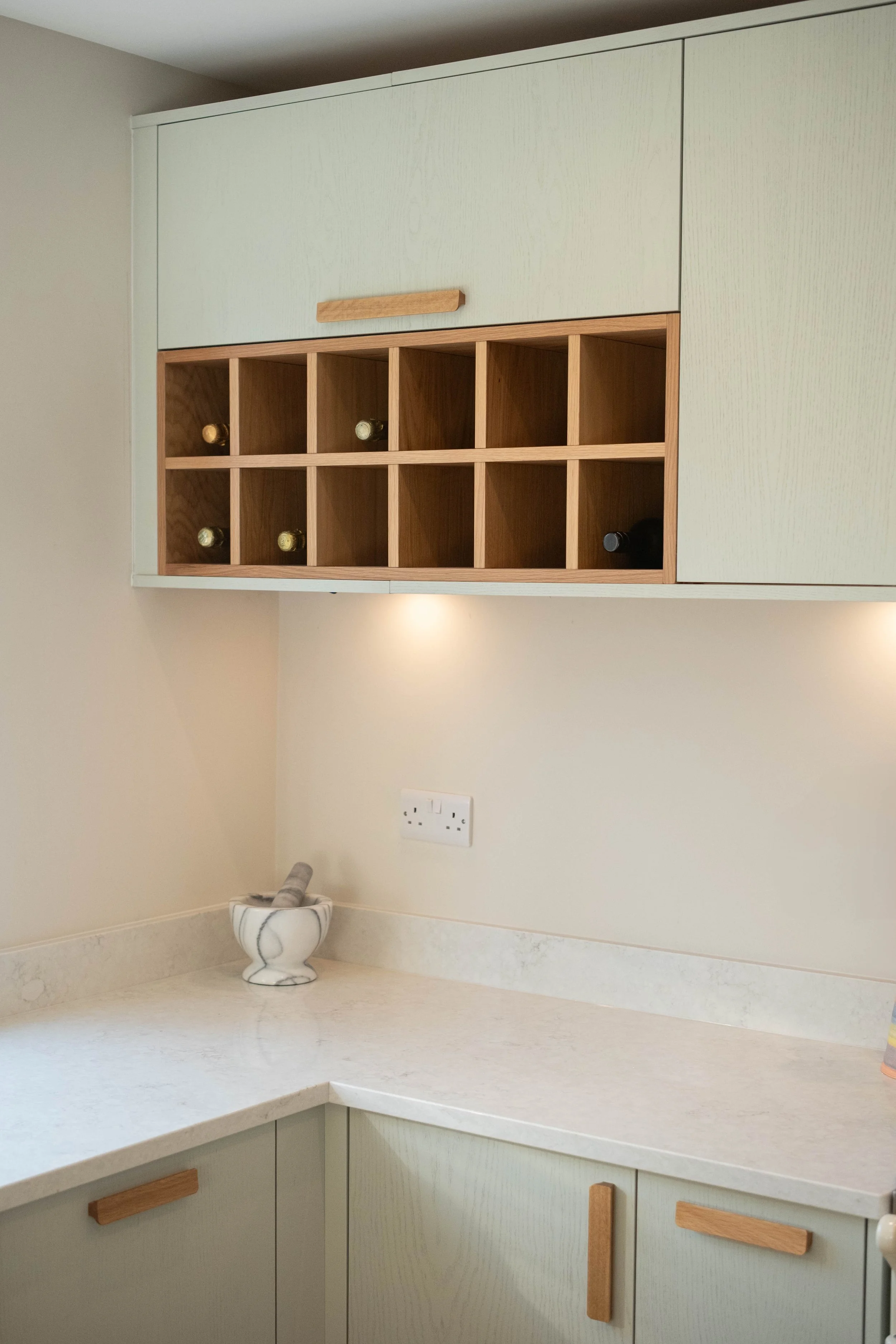 Kitchen cabinets with wooden handles, a countertop, a marble mortar and pestle on the countertop, and a wall outlet.