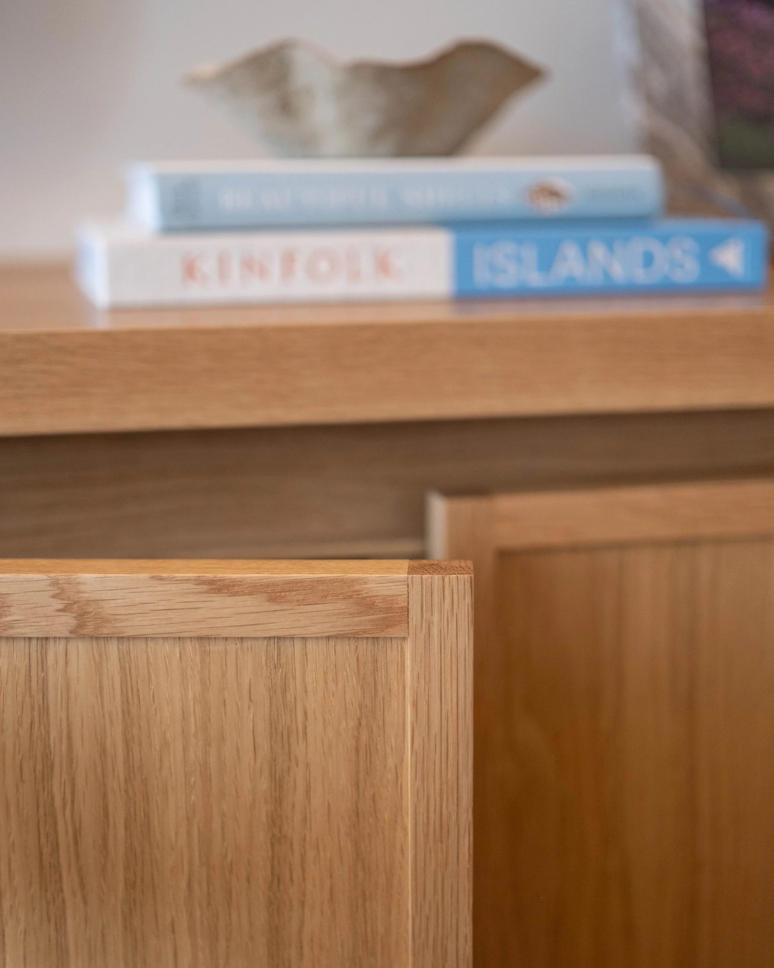 Two books, one titled 'KINFOLK' and the other 'ISLANDS,' placed on a wooden surface with a decorative dried flower above them.