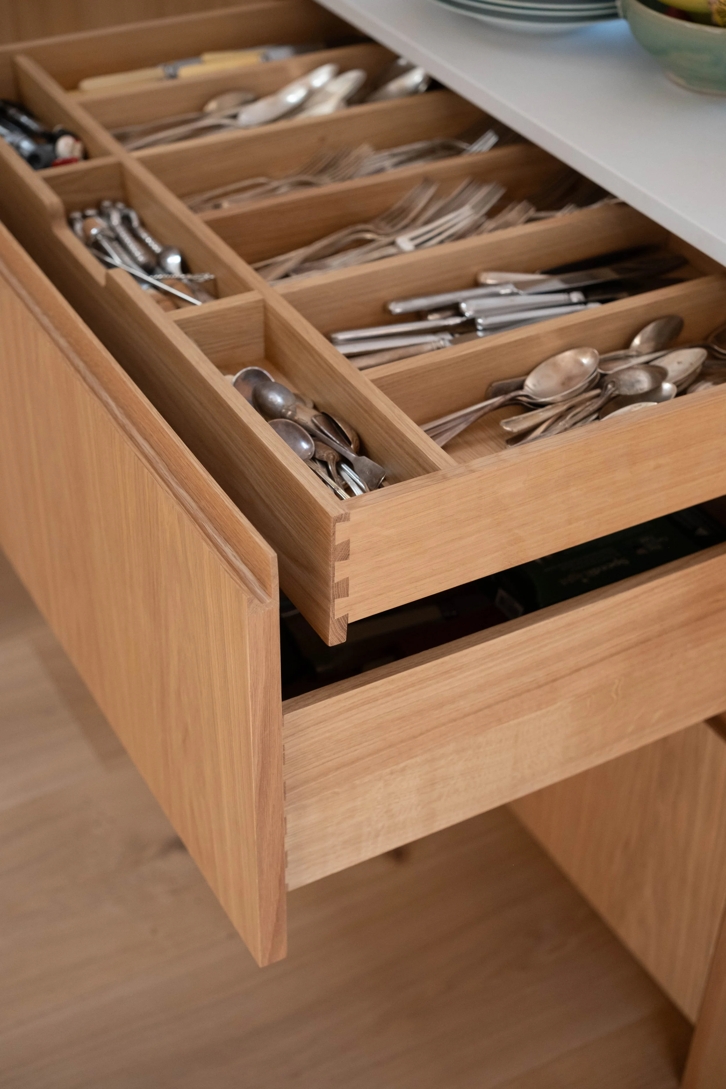 Open wooden drawer filled with neatly arranged silverware, including spoons, forks, and knives.
