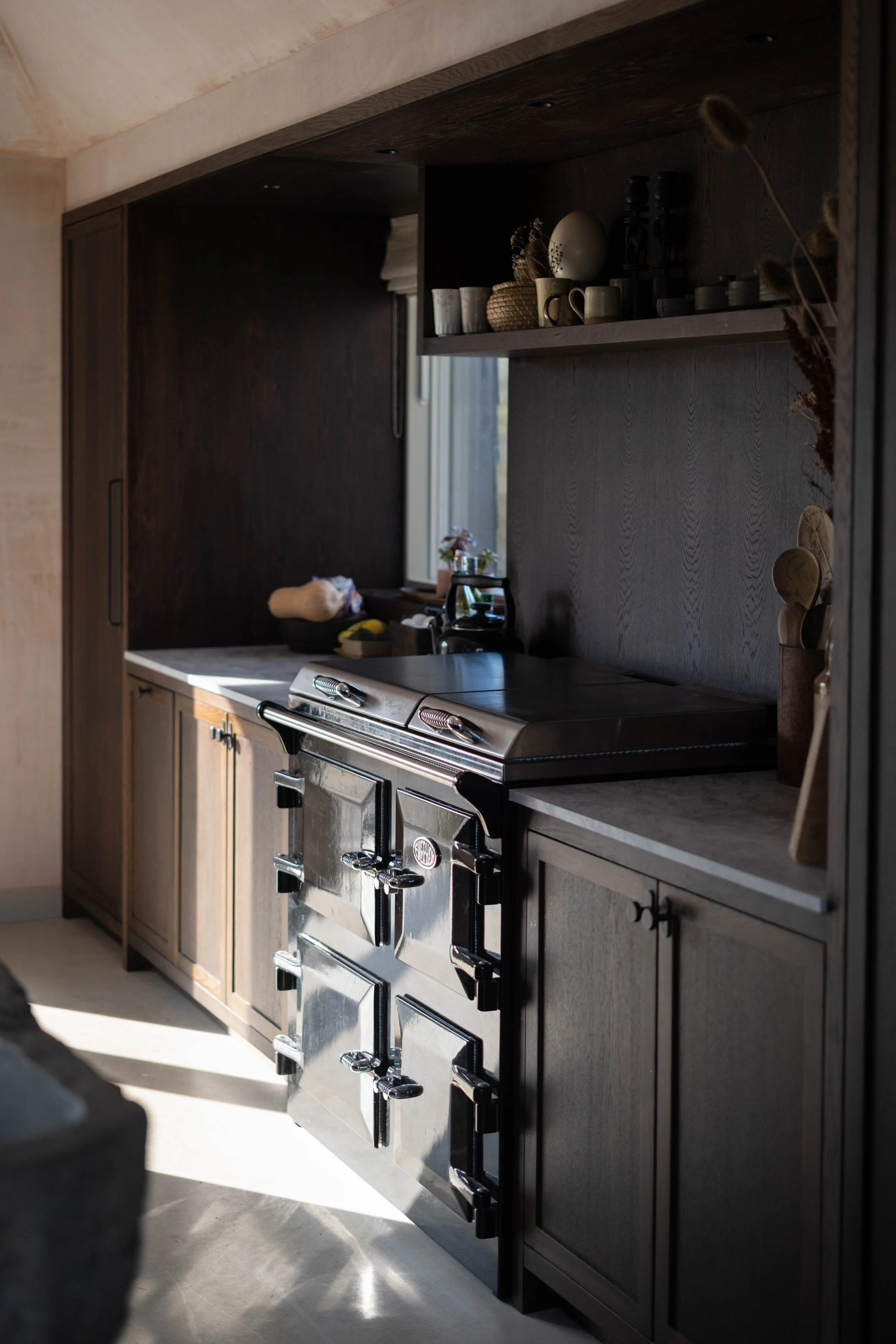 A kitchen with dark wood cabinets, a stainless steel oven, and a countertop with miscellaneous items and a window in the background.