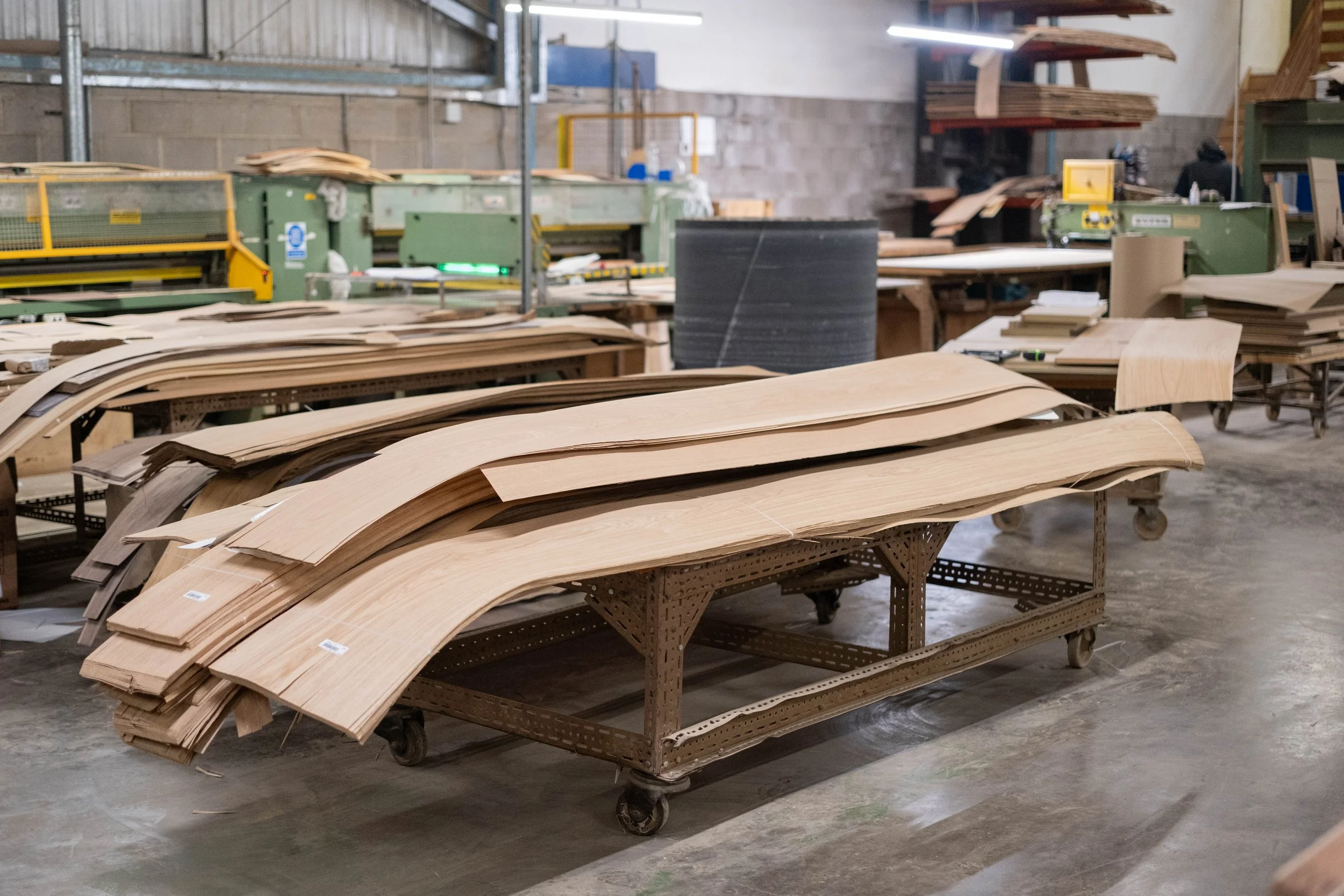 A woodworking workshop with several piles of wooden planks and presses on carts in an industrial setting.